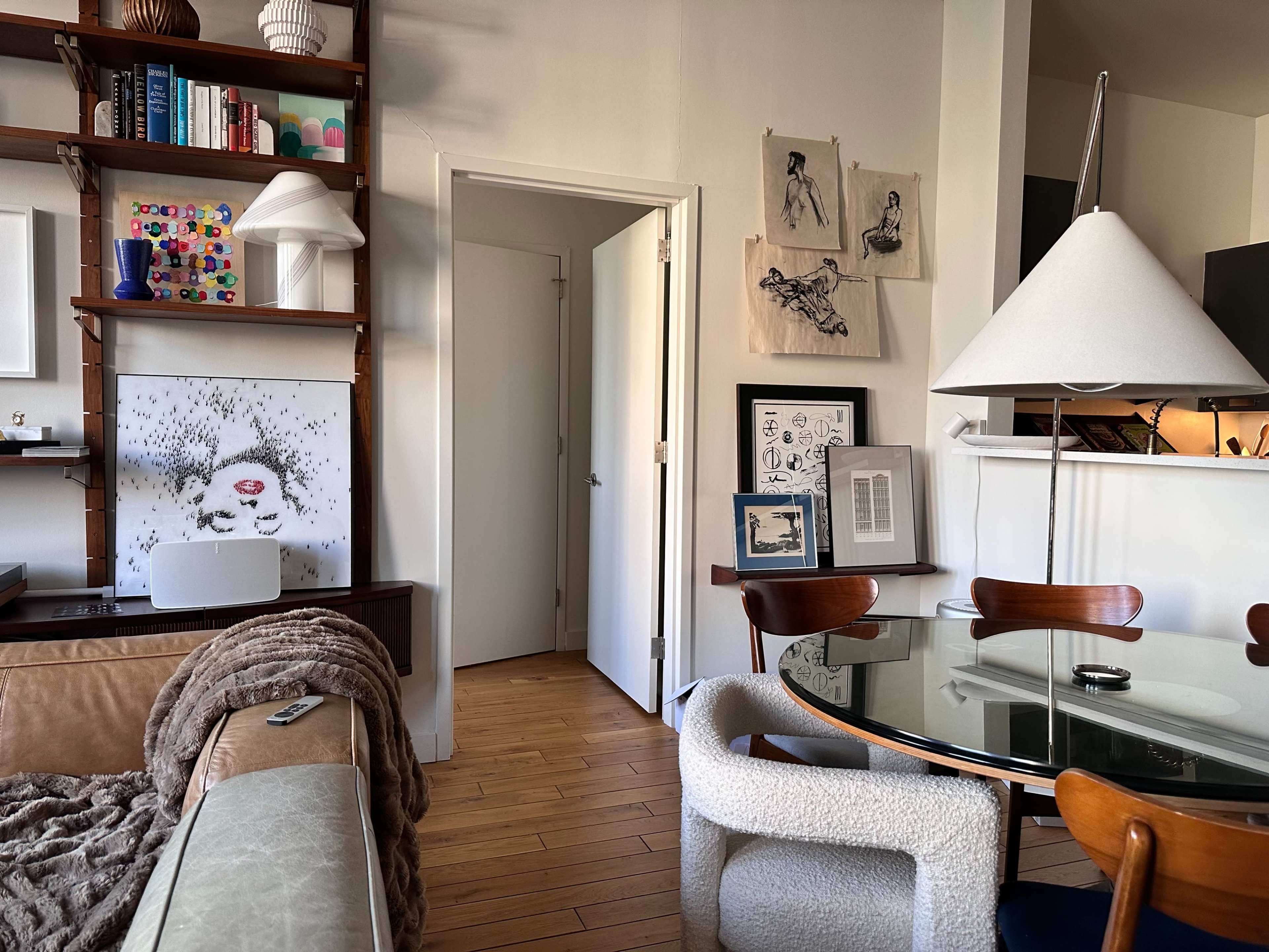 The scene features a modern living space with a cozy sofa, a round glass dining table, and a doorway leading to another room, accented by artwork on the walls.