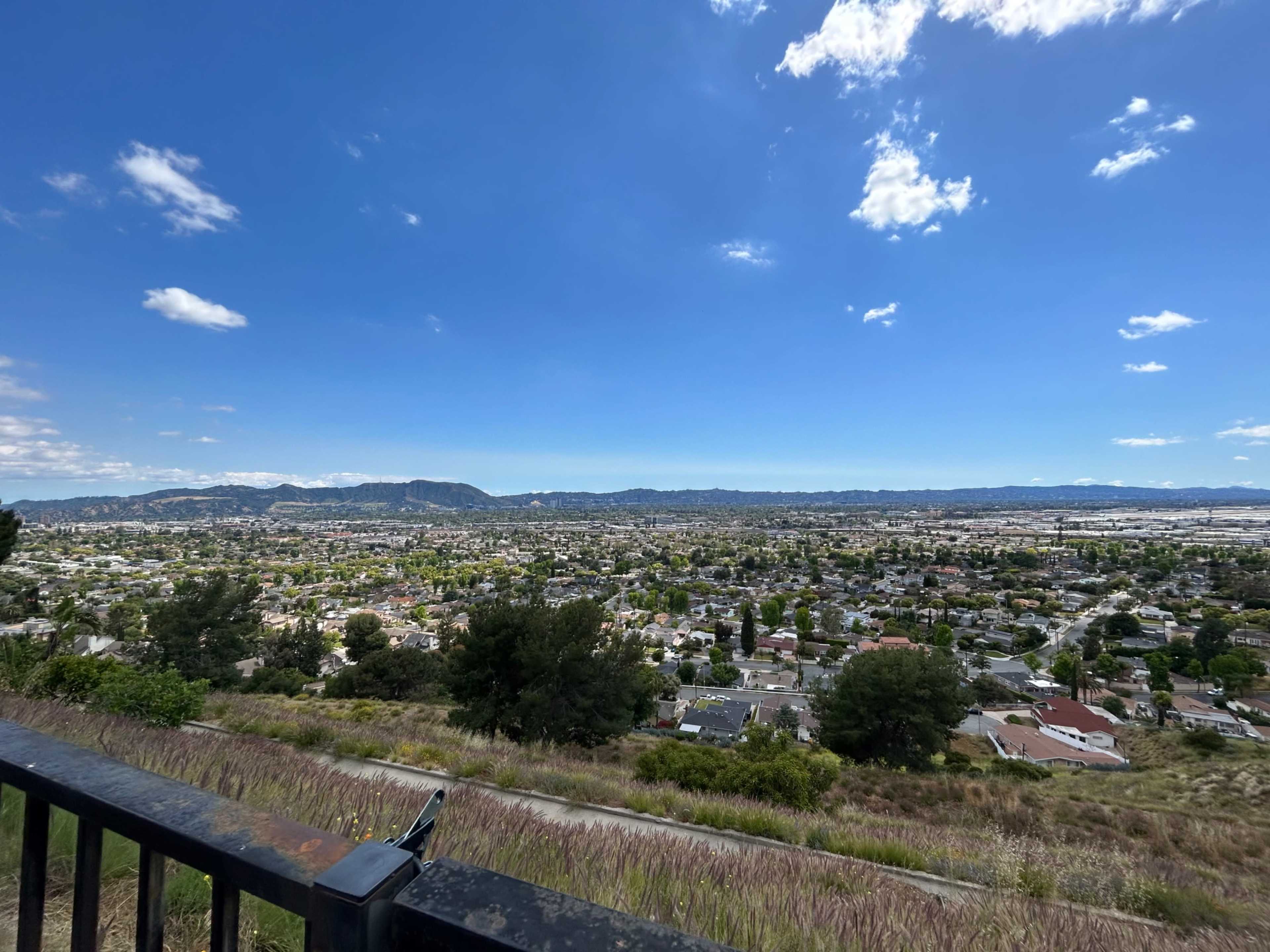 A panoramic view of a cityscape with residential areas and distant mountains under a partly cloudy sky.