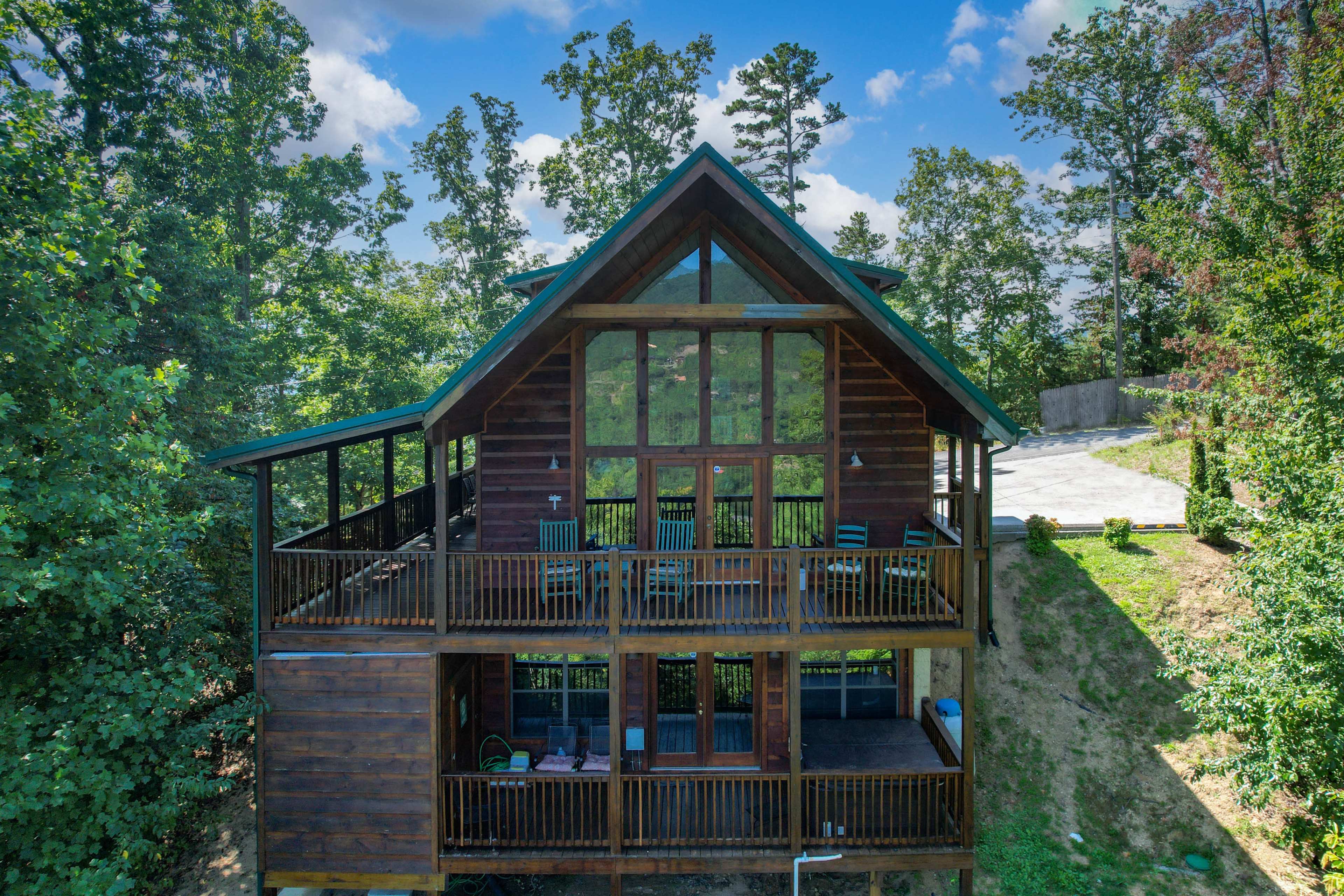 A large wooden cabin with a steep roof and multiple balconies is situated among trees on a hillside.