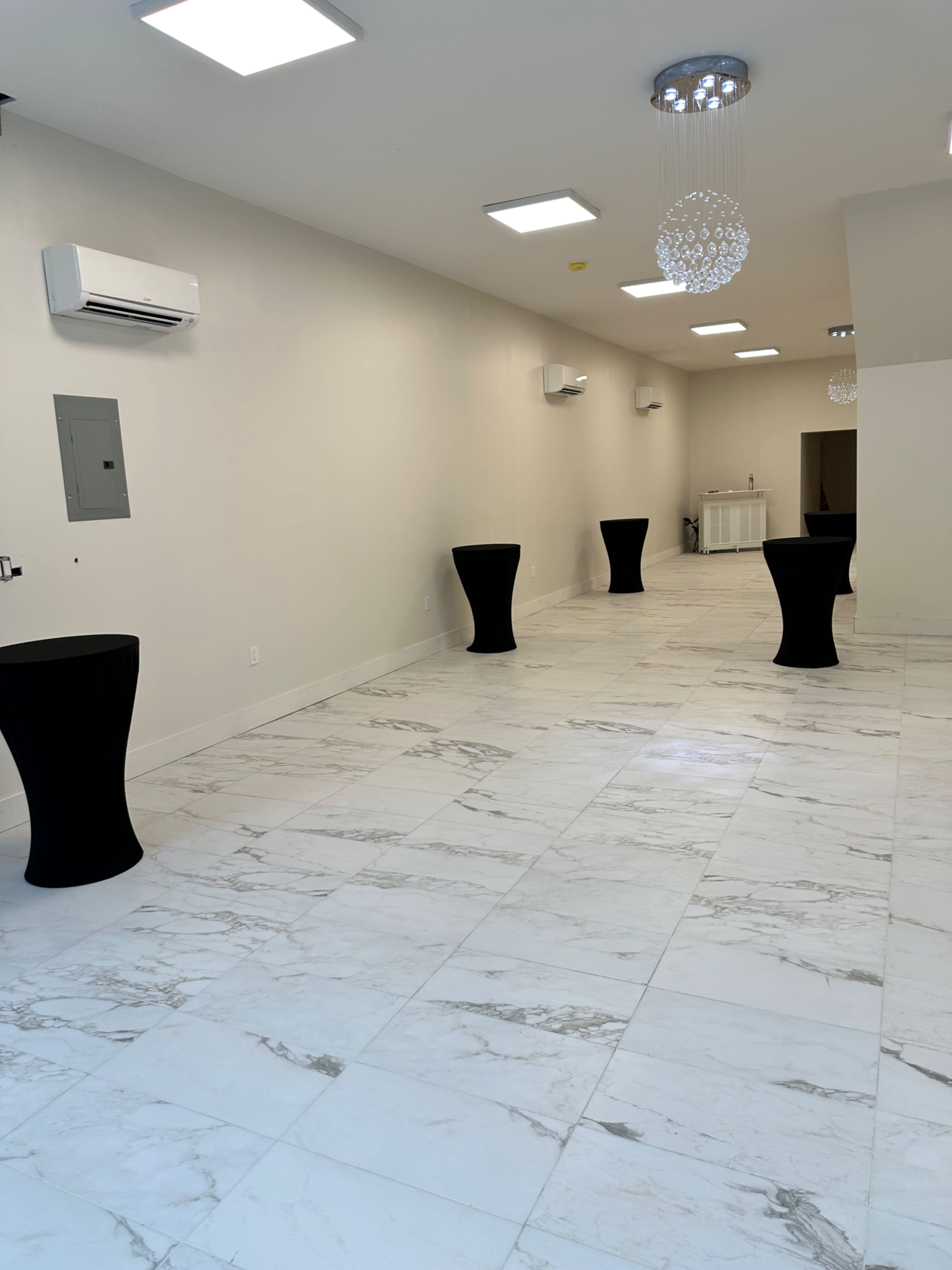 An empty room with white marble tile flooring and several black high-top tables positioned throughout.