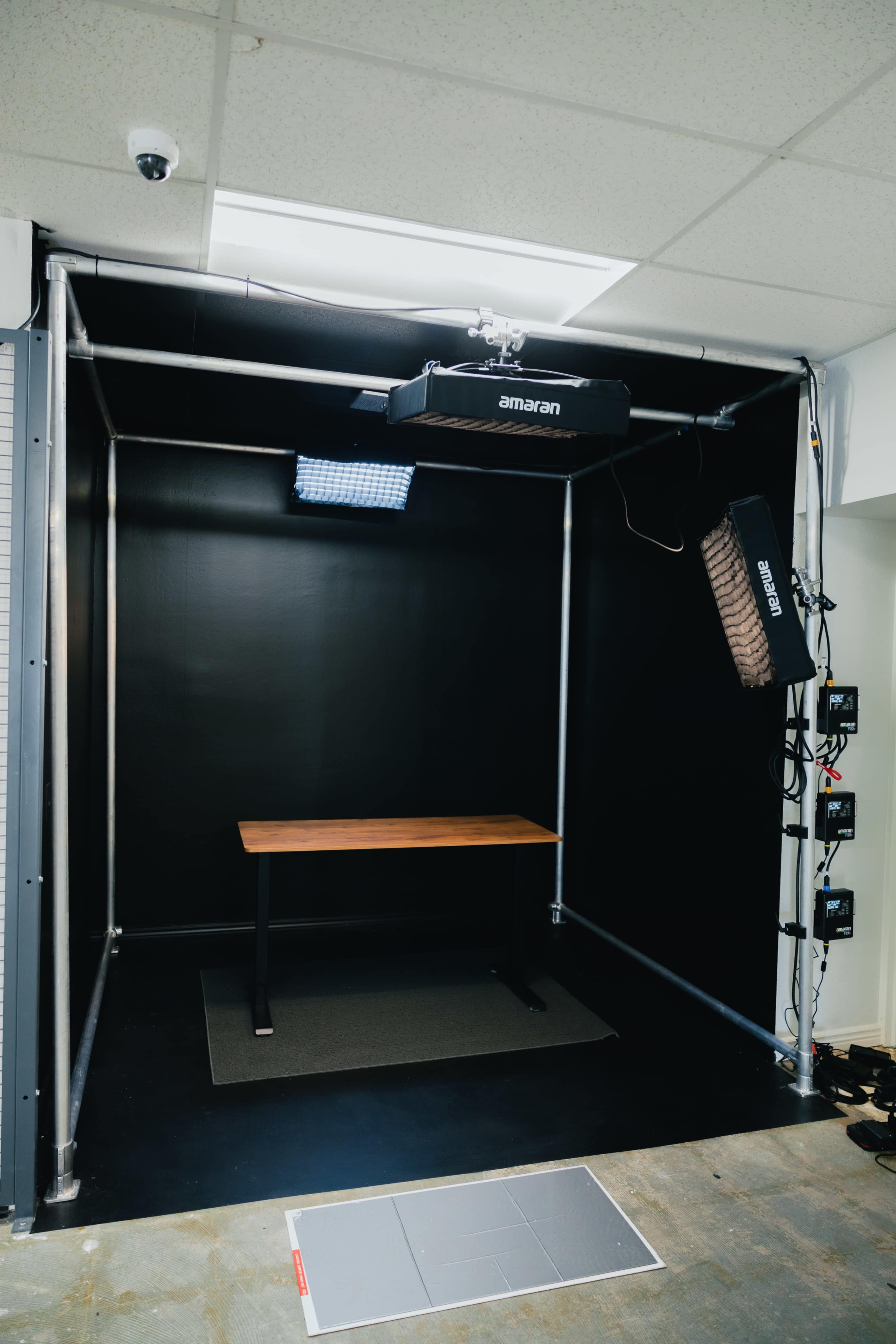 A photography studio with a black backdrop, a wooden table in the center, and positioned lighting equipment.