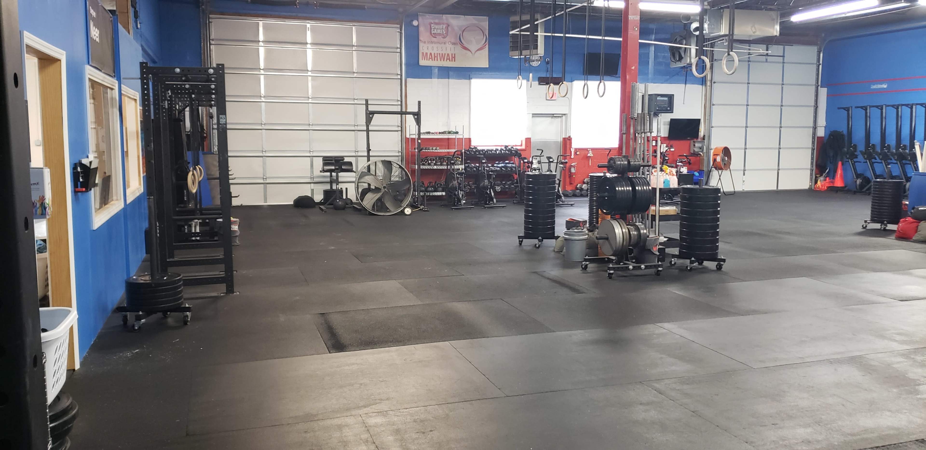 A large, empty gym space with various exercise equipment arranged along the walls, including weights, benches, and conditioning tools.