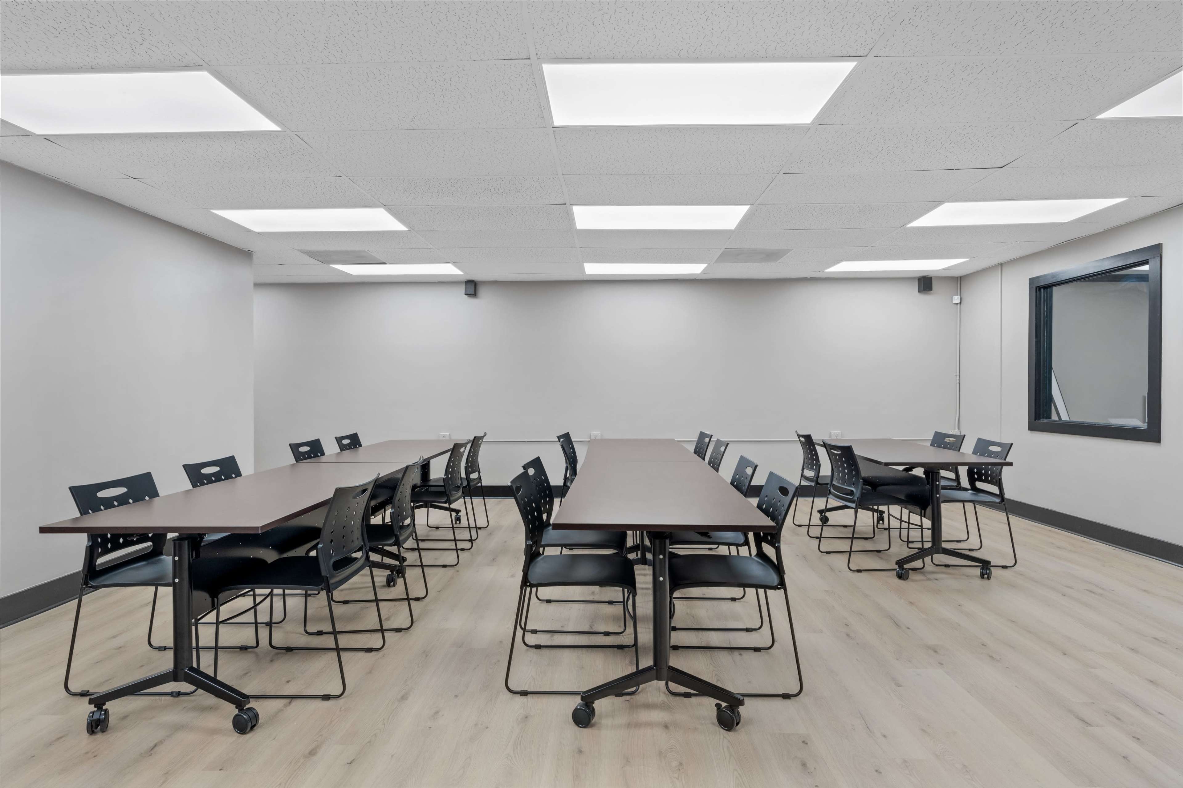 A spacious meeting room equipped with several tables and chairs arranged neatly in rows on a light-colored wooden floor.