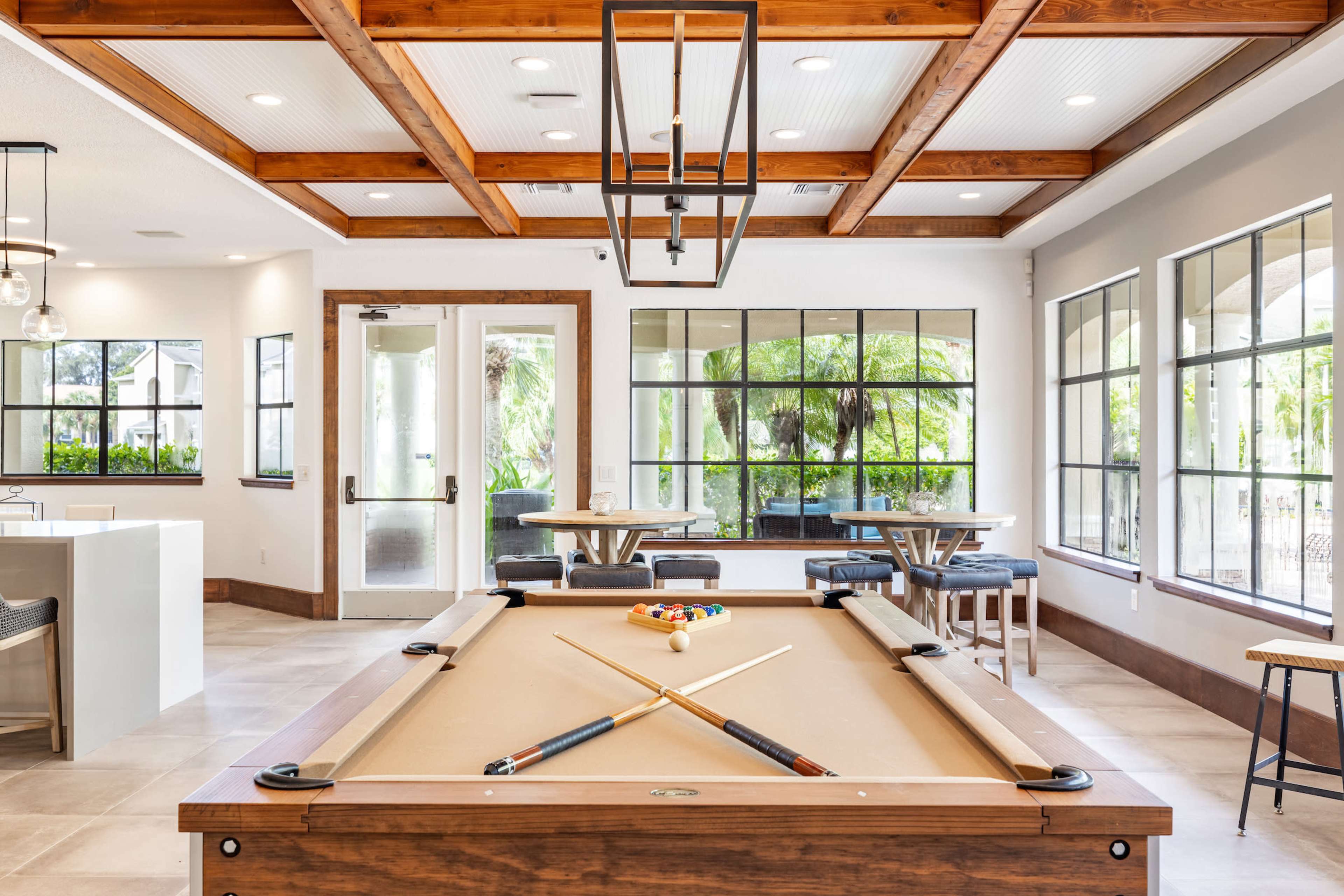 A billiards table in an indoor lounge area featuring large windows and wooden beams in the ceiling.