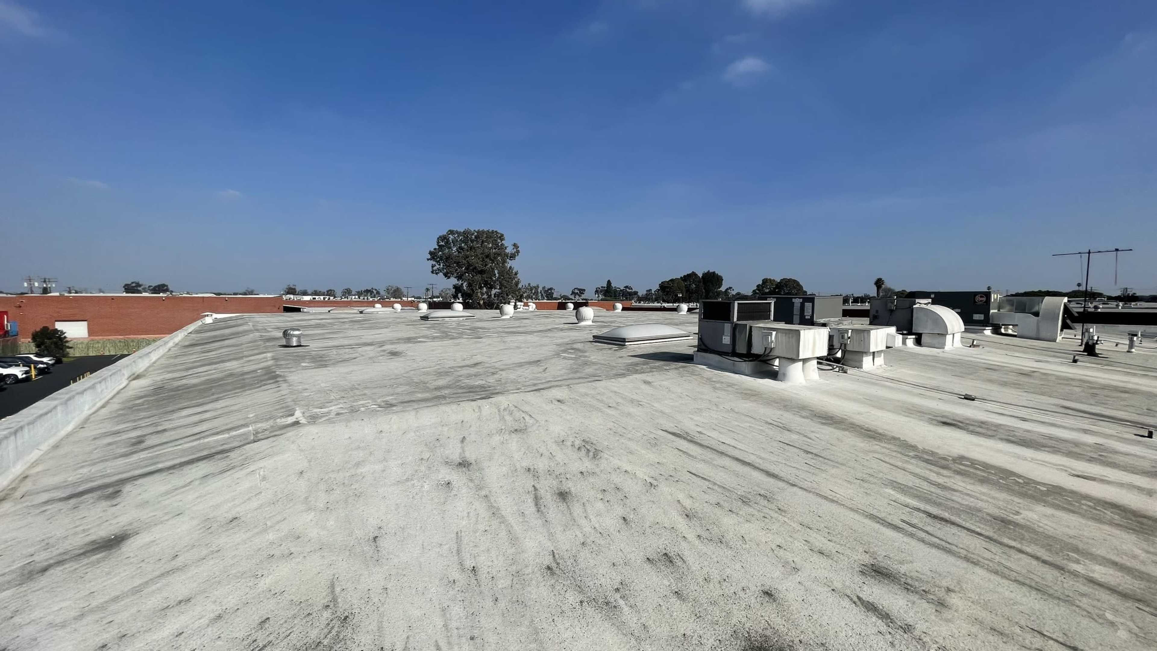 A flat rooftop with several ventilation units and a tree visible in the background under a clear sky.