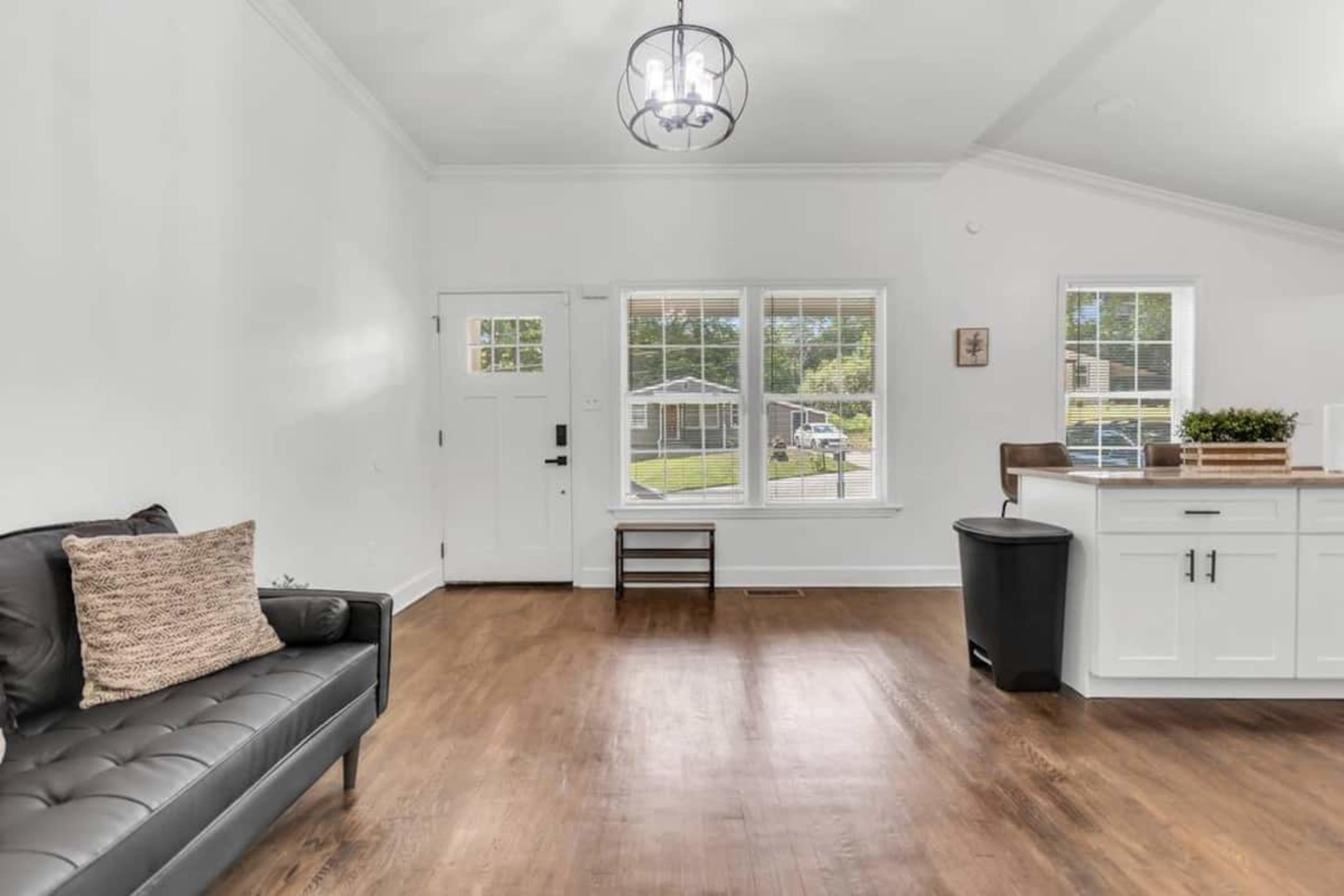 A bright, open living space features a black sofa, large windows, and a view of an outdoor area.