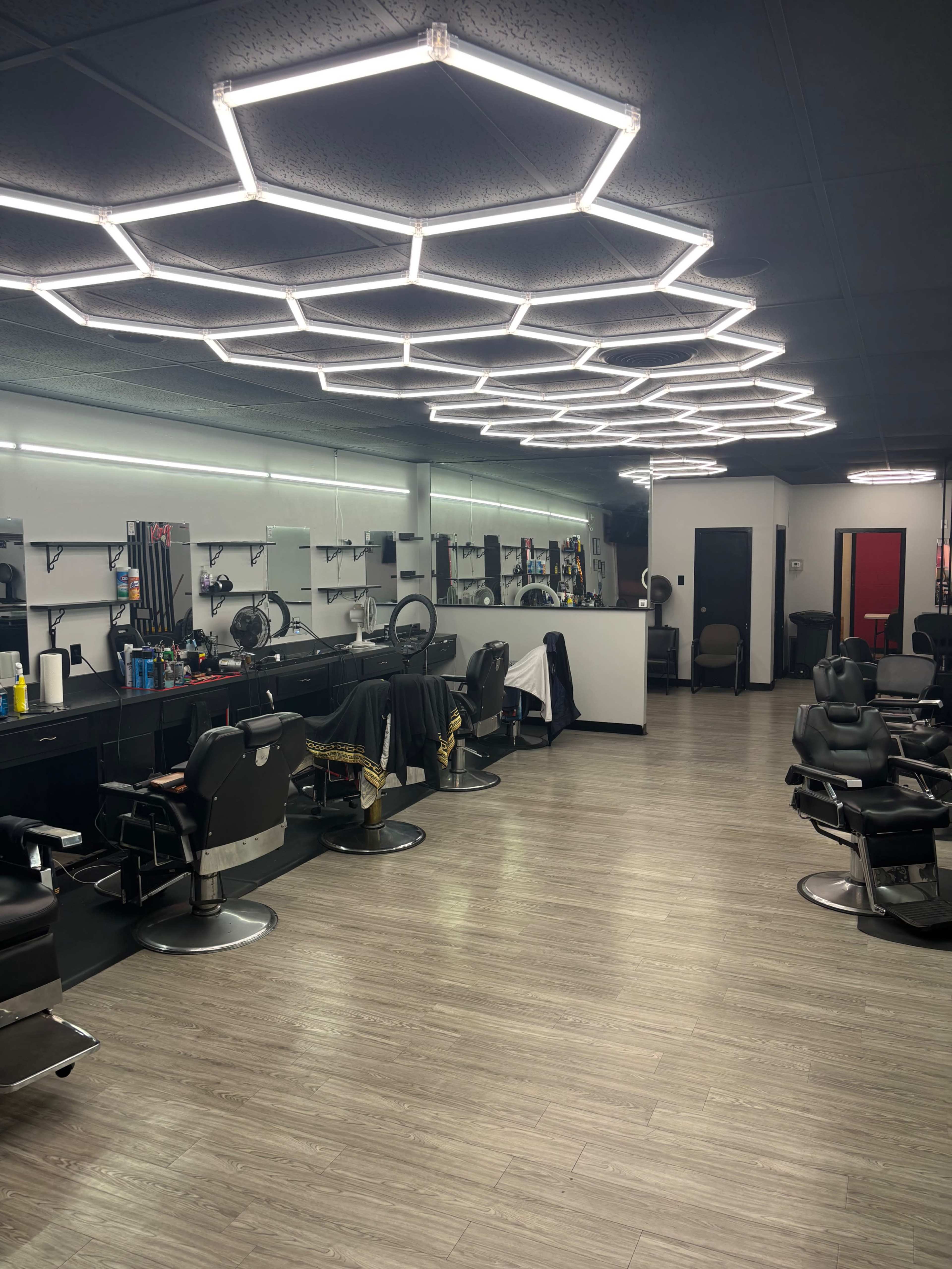 The image shows a modern barbershop interior with multiple styling stations, equipped chairs, and a unique hexagonal light fixture on the ceiling.