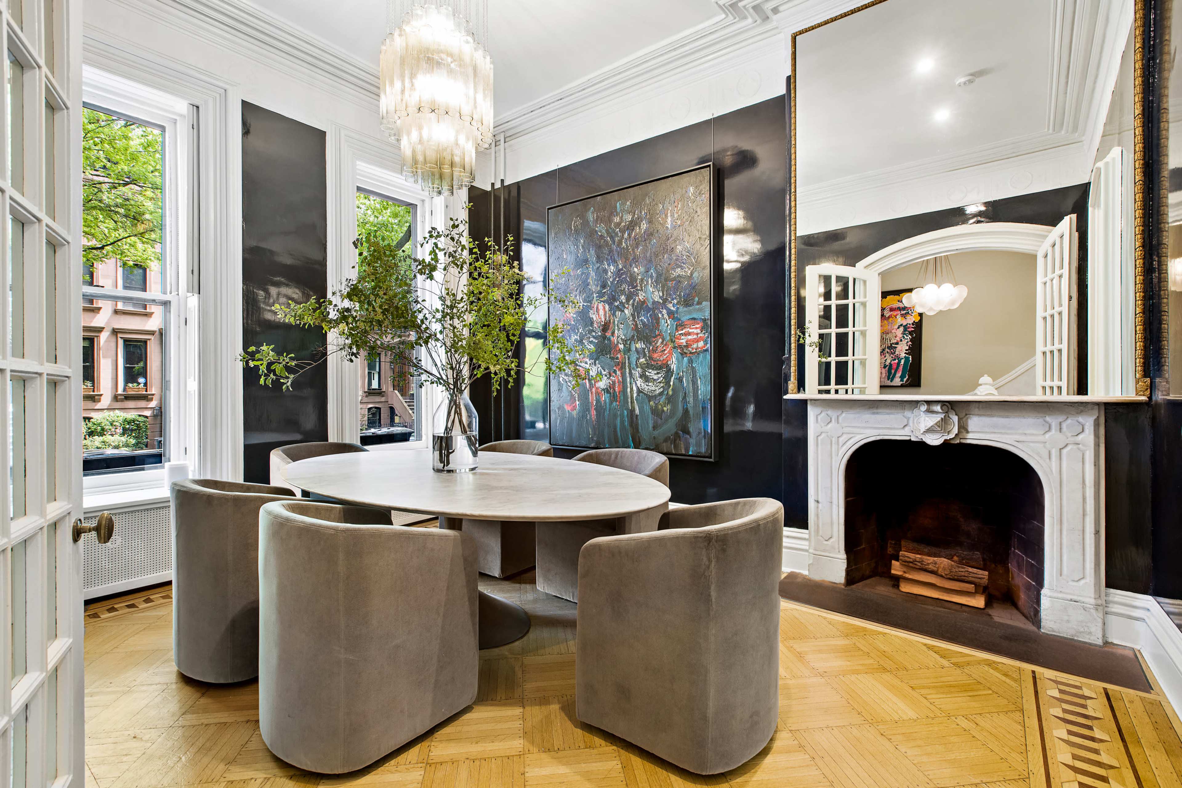 A stylish dining room featuring a round table surrounded by upholstered chairs, a large artwork on the wall, and a fireplace with a decorative mirror above it.