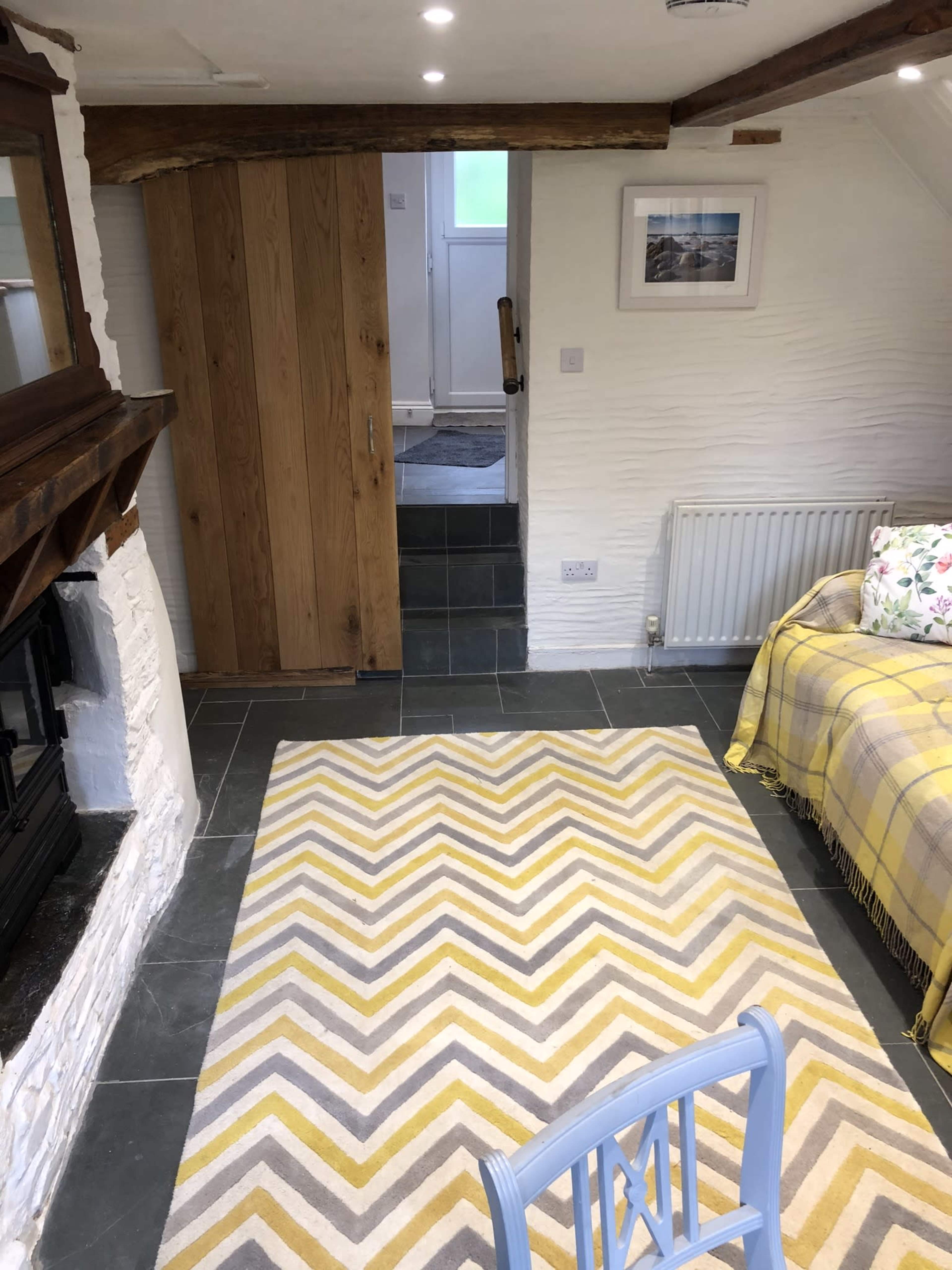 A cozy room with a stone floor, a patterned rug, wooden beams, and a staircase leading to another area.