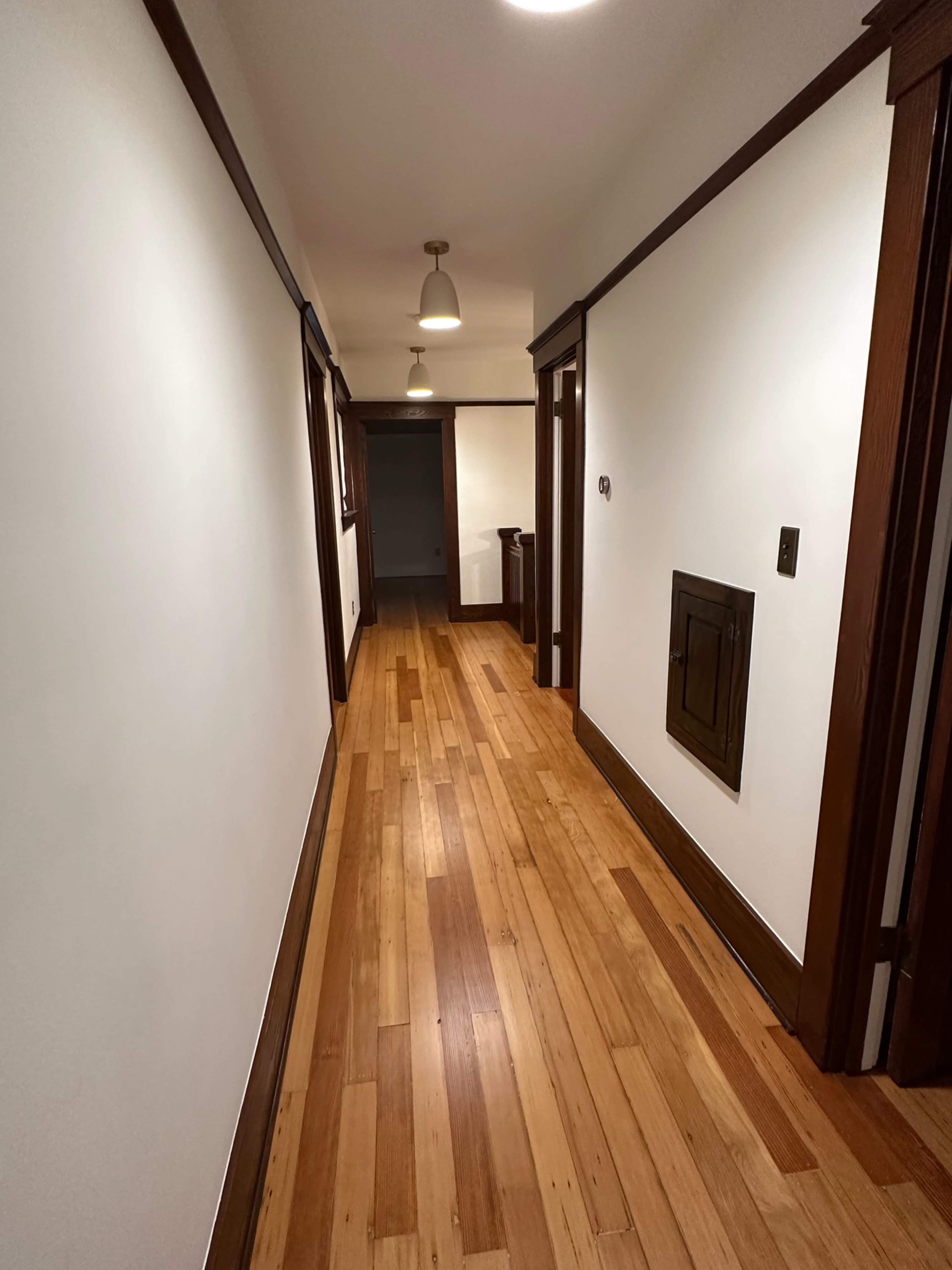 A long, narrow hallway with wooden flooring and white walls, featuring doors on either side.
