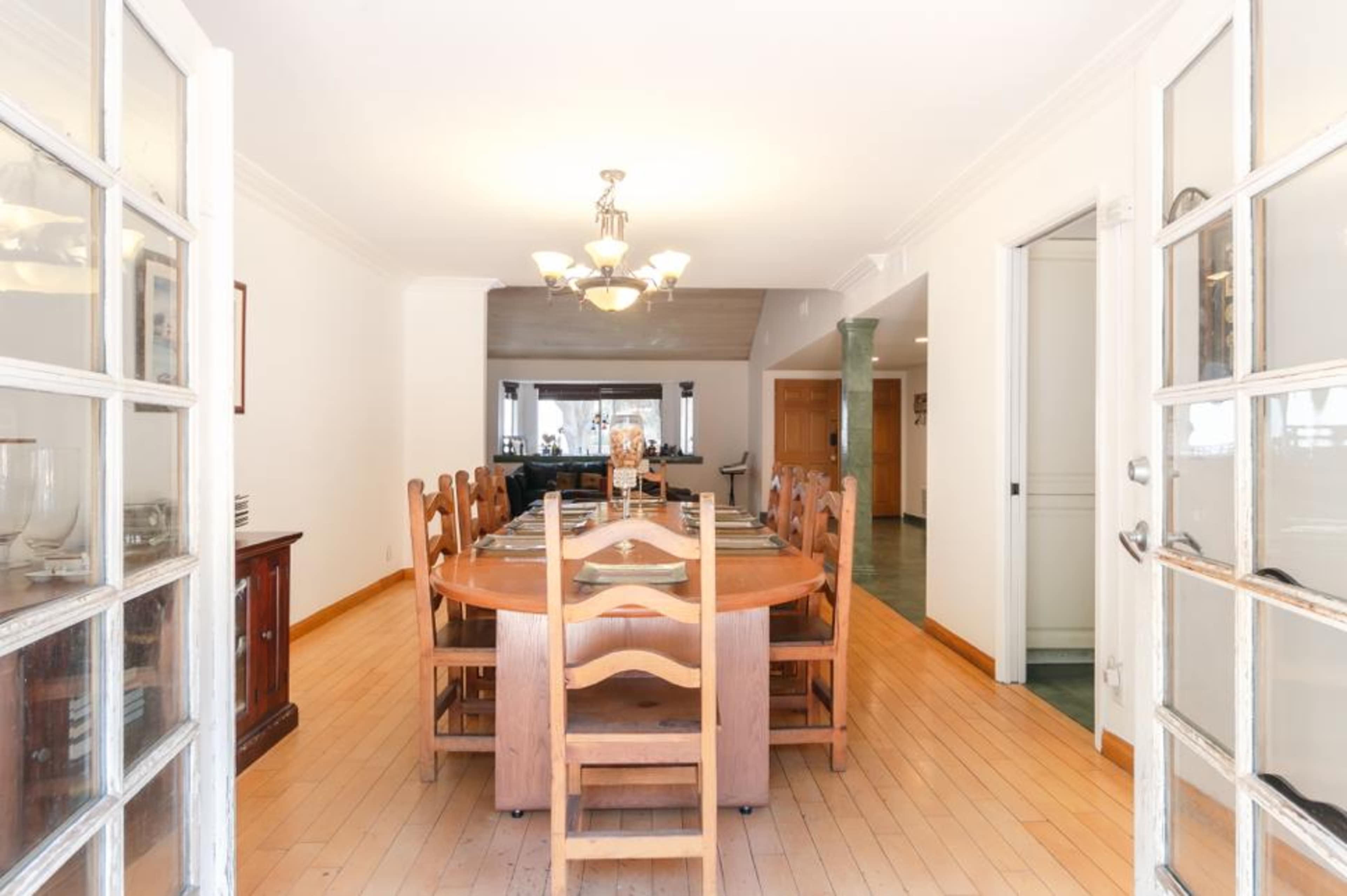A long wooden dining table is set for a meal in a well-lit room with glass doors leading to the dining area.