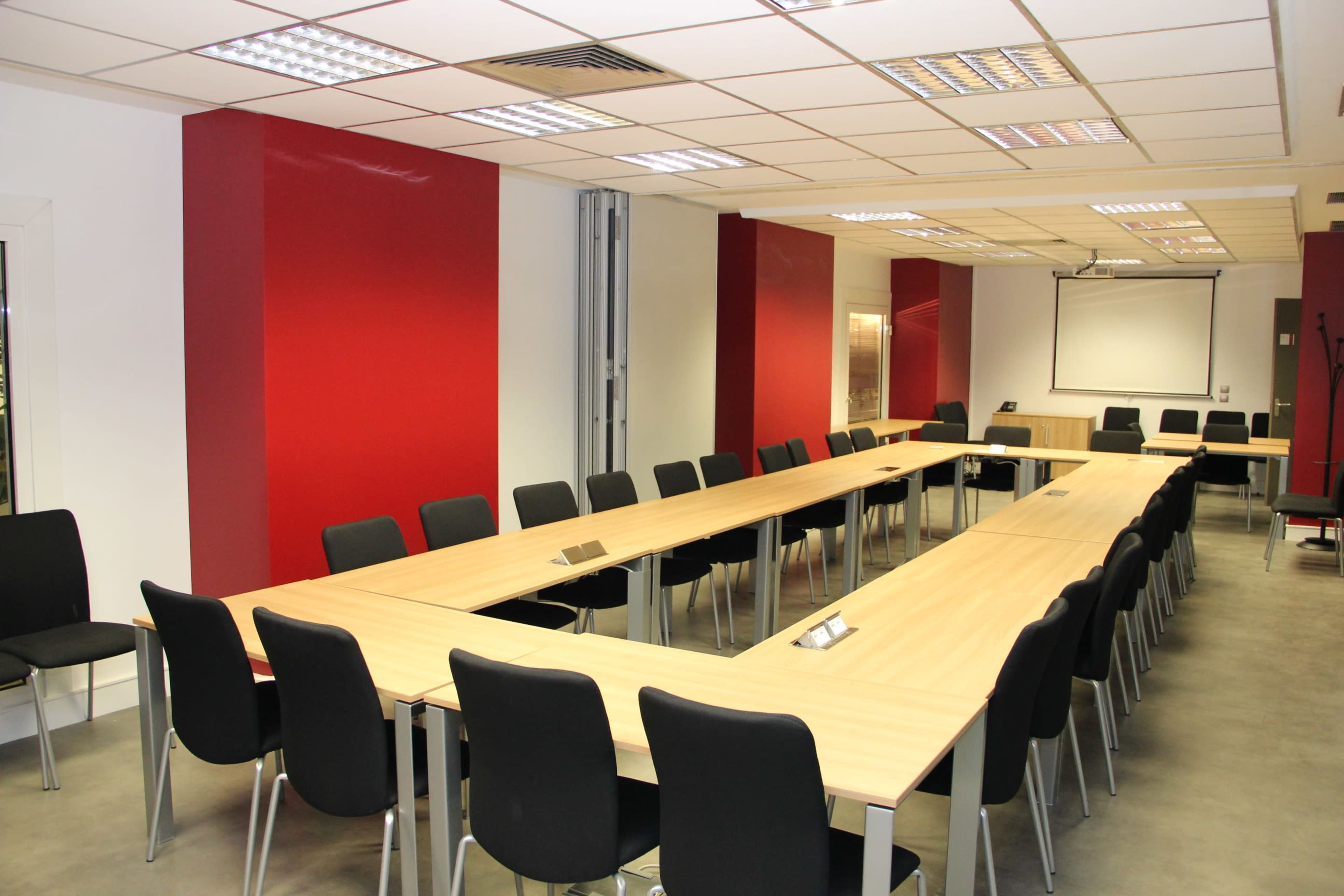 A modern conference room with a long, rectangular table surrounded by black chairs and red accent walls.