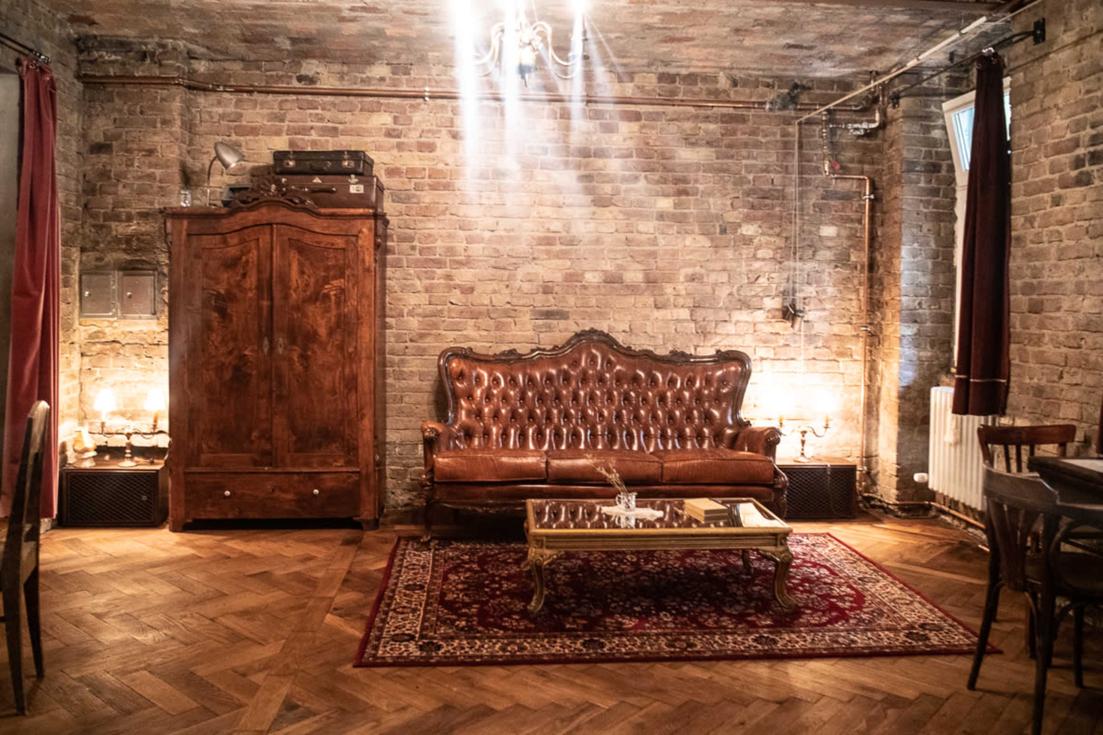 A rustic room with exposed brick walls, featuring a vintage leather sofa and a wooden armoire, illuminated by soft lighting.