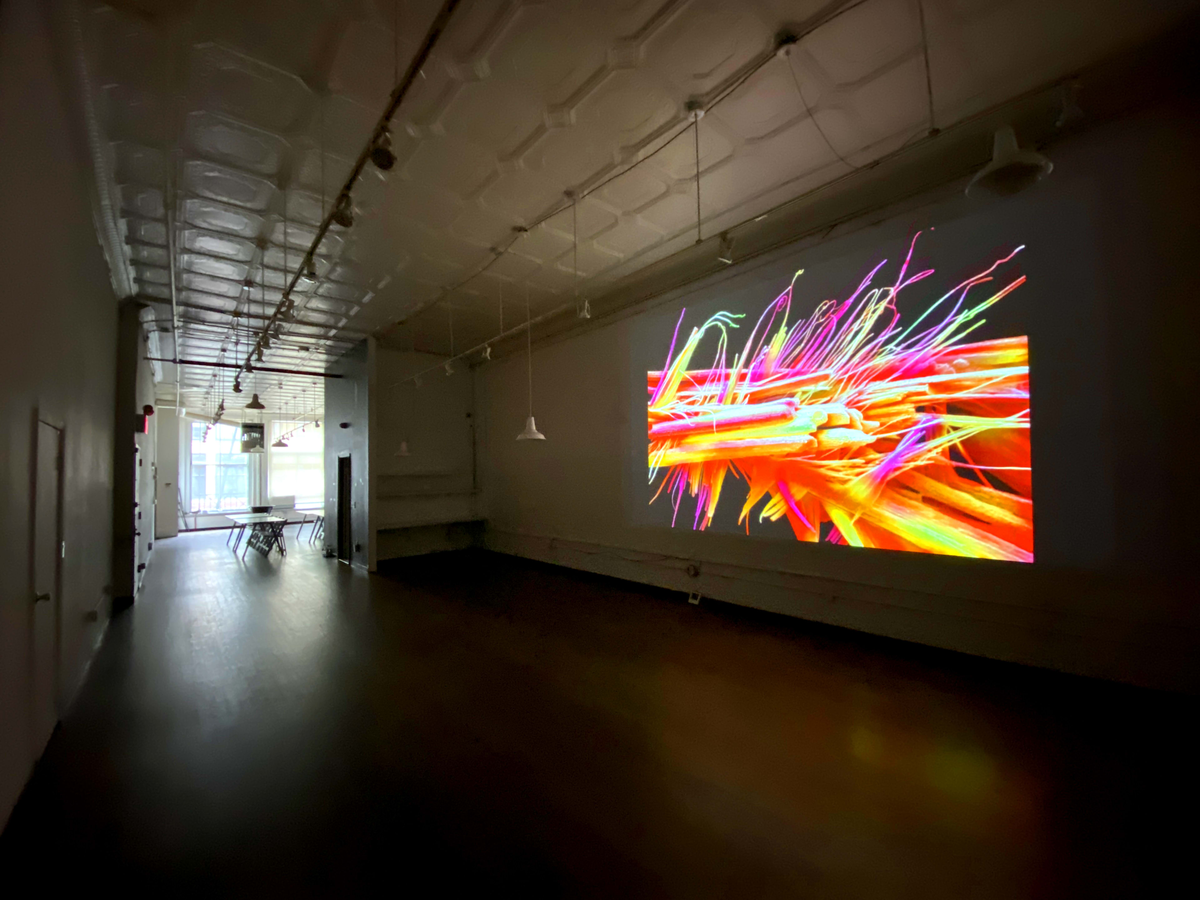 A brightly colored digital art piece is displayed on a wall in a spacious, dimly lit gallery.