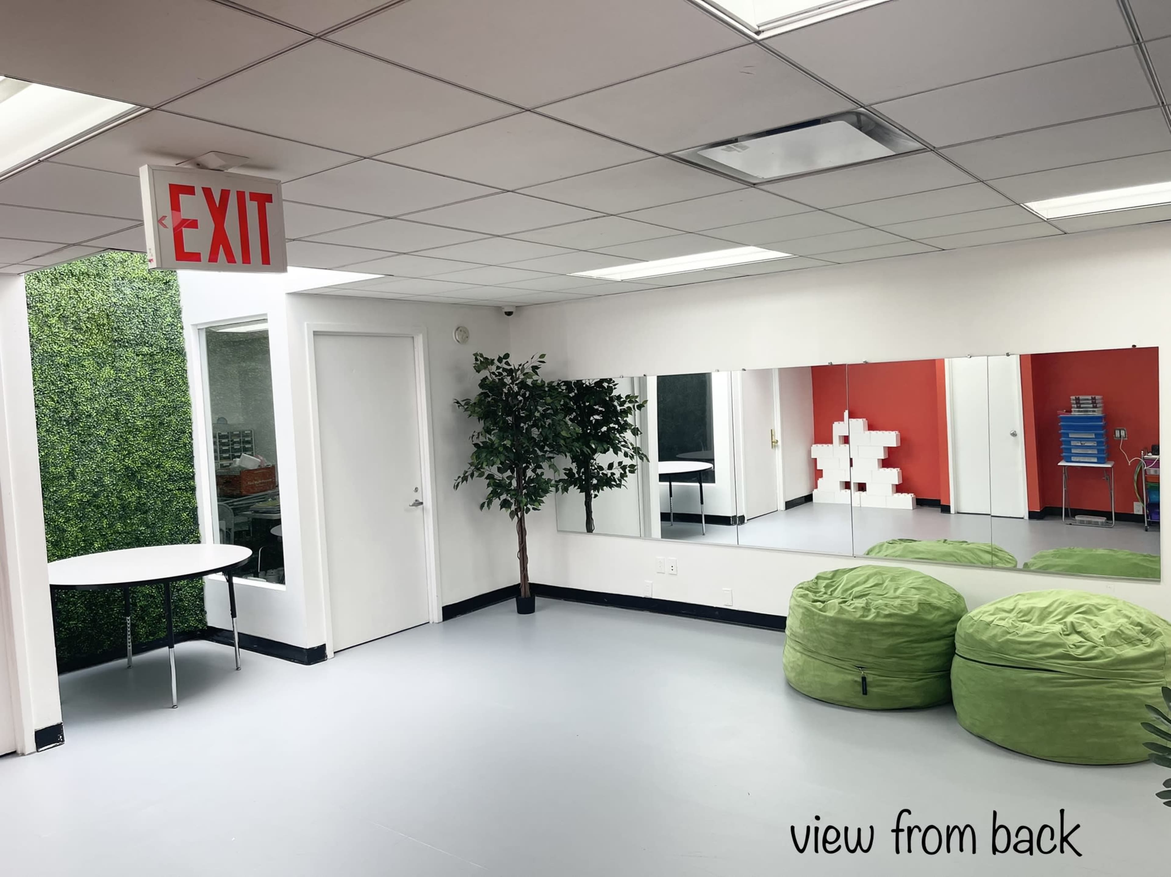 A brightly lit room with a green wall, a table, a large mirror, and two bean bags.