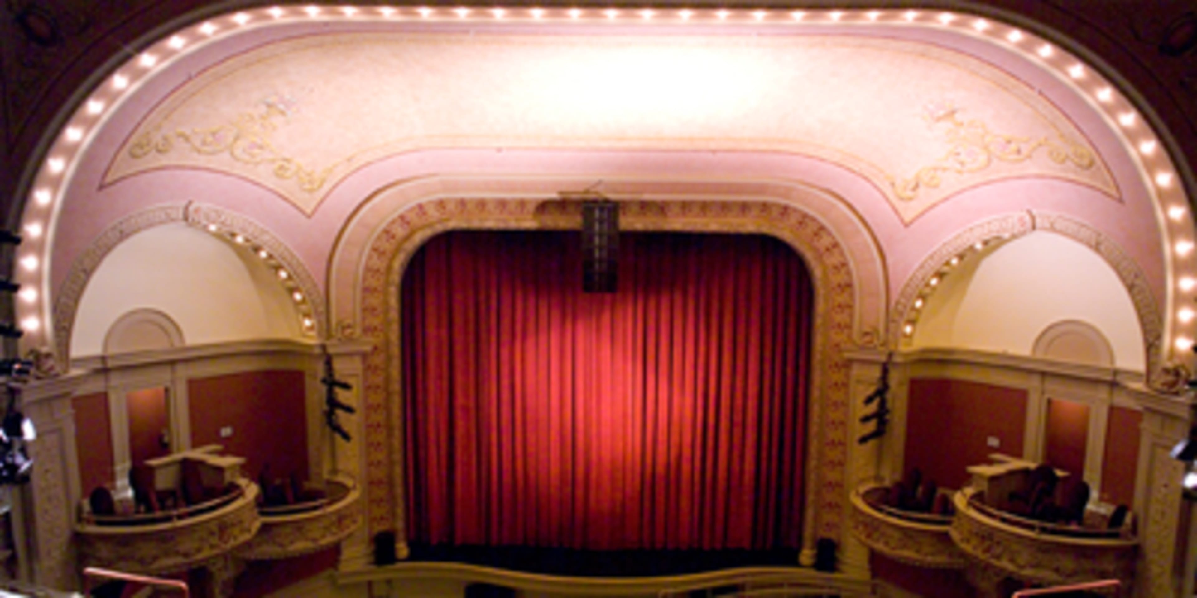 The image shows the interior of a theater with a red curtain and ornate architecture.