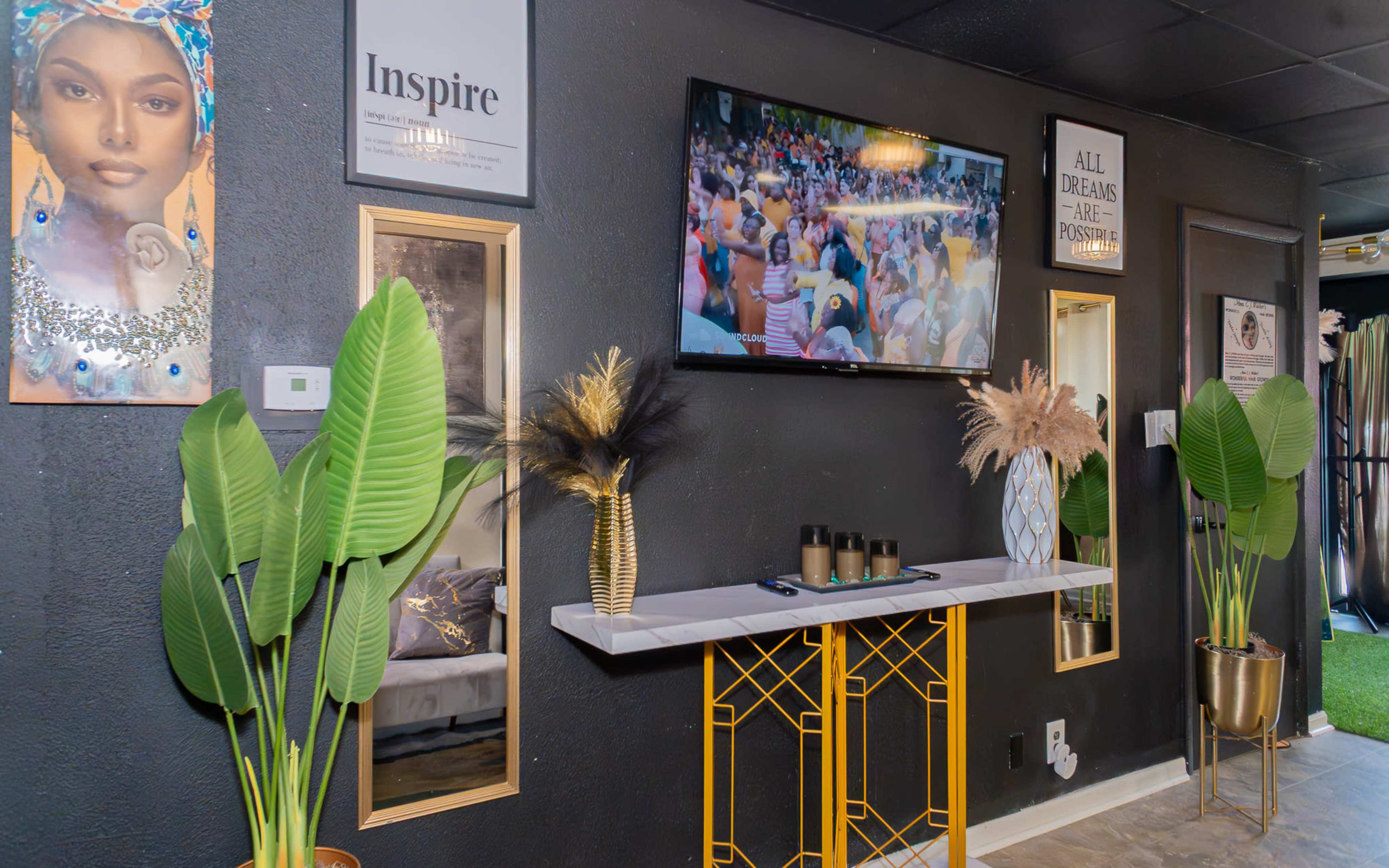 The image shows a stylish interior featuring a television mounted on a black wall, decorative plants, and framed inspirational quotes.