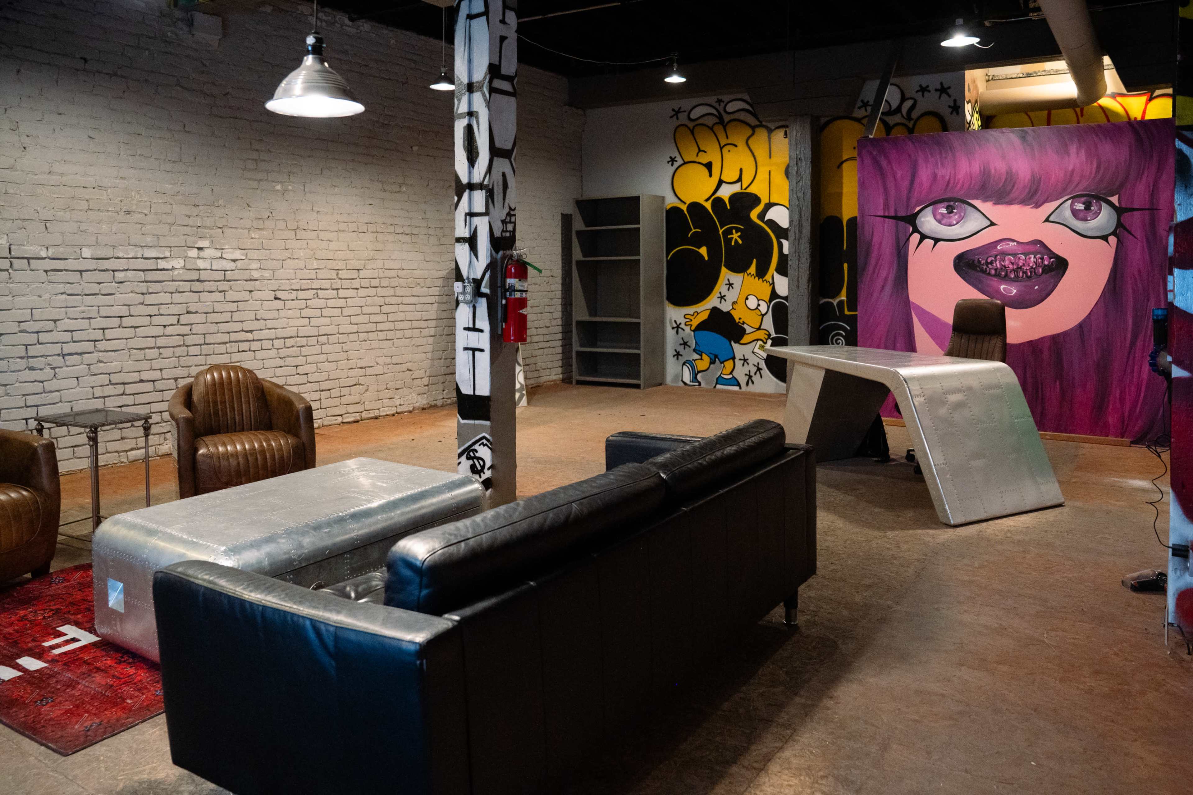 The image shows a modern lounge area with leather seating, unique tables, and vibrant graffiti-style artwork on the walls.