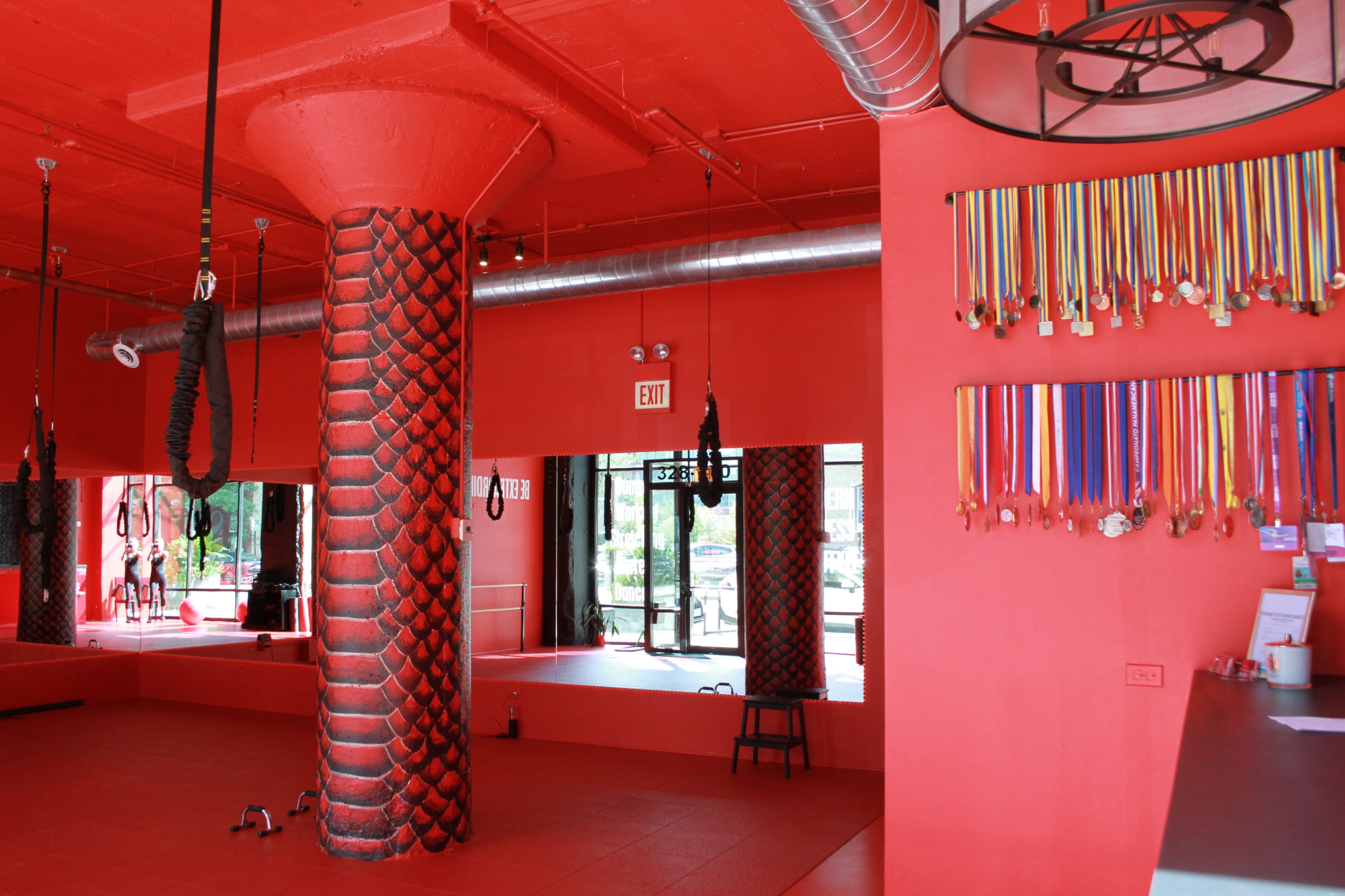 The interior of a martial arts studio features bright red walls, a textured column, hanging workout equipment, and a display of colorful medals.