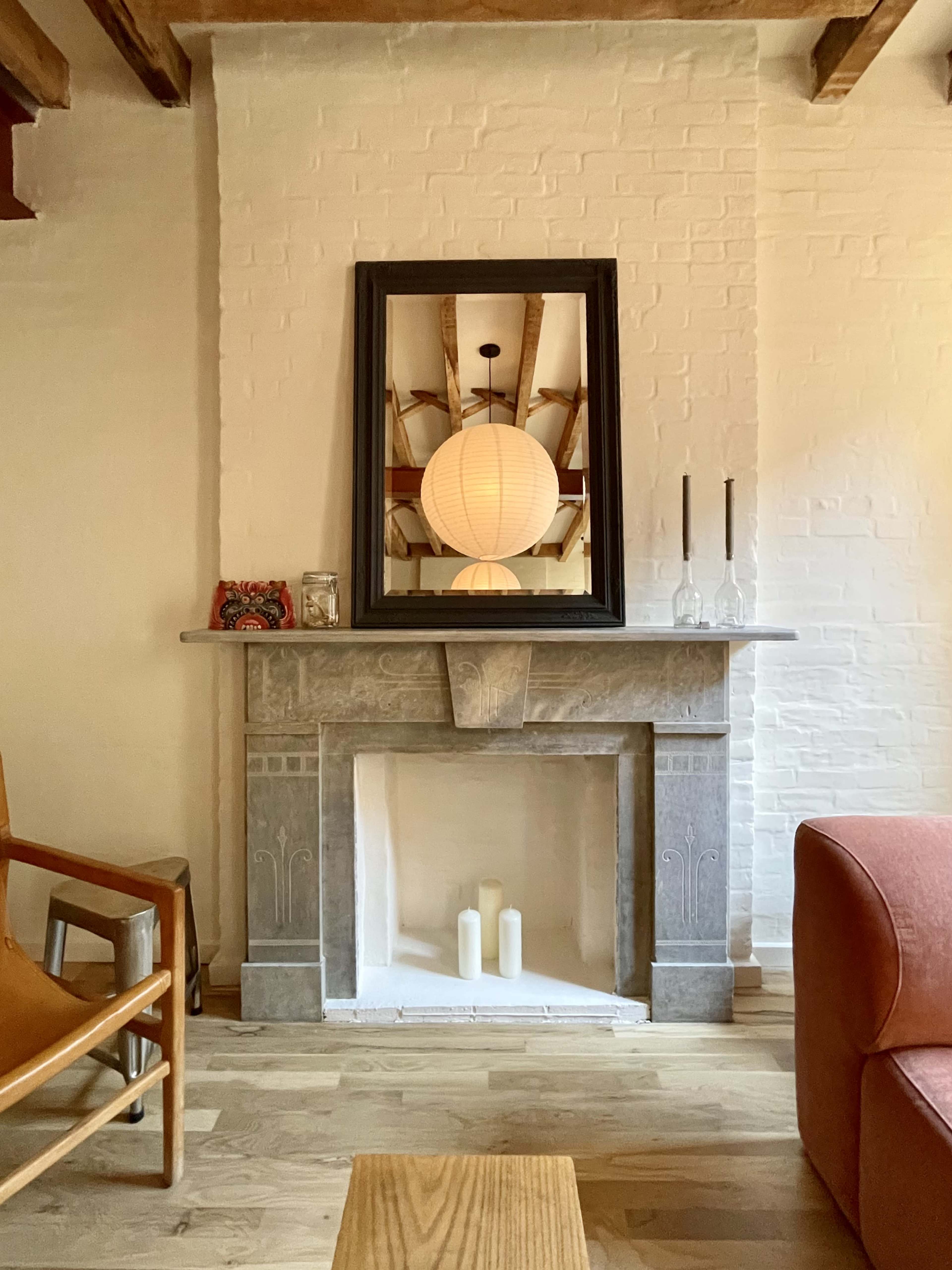 The image shows a living room with a stone fireplace, a round lantern hanging from the ceiling, and a wooden chair beside a low table.