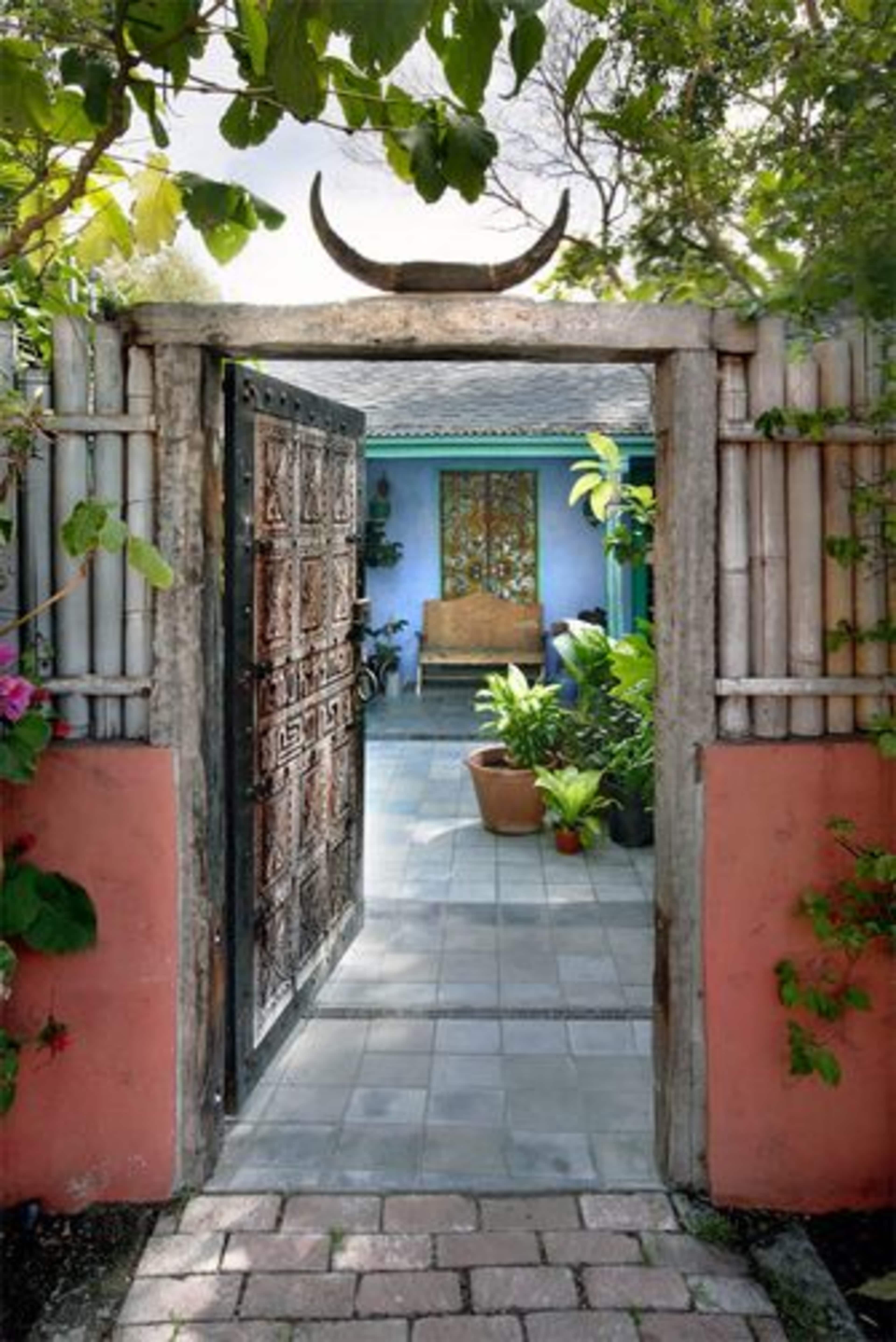 A wooden gate opening into a courtyard with tiled flooring, surrounded by plants and colorful walls.