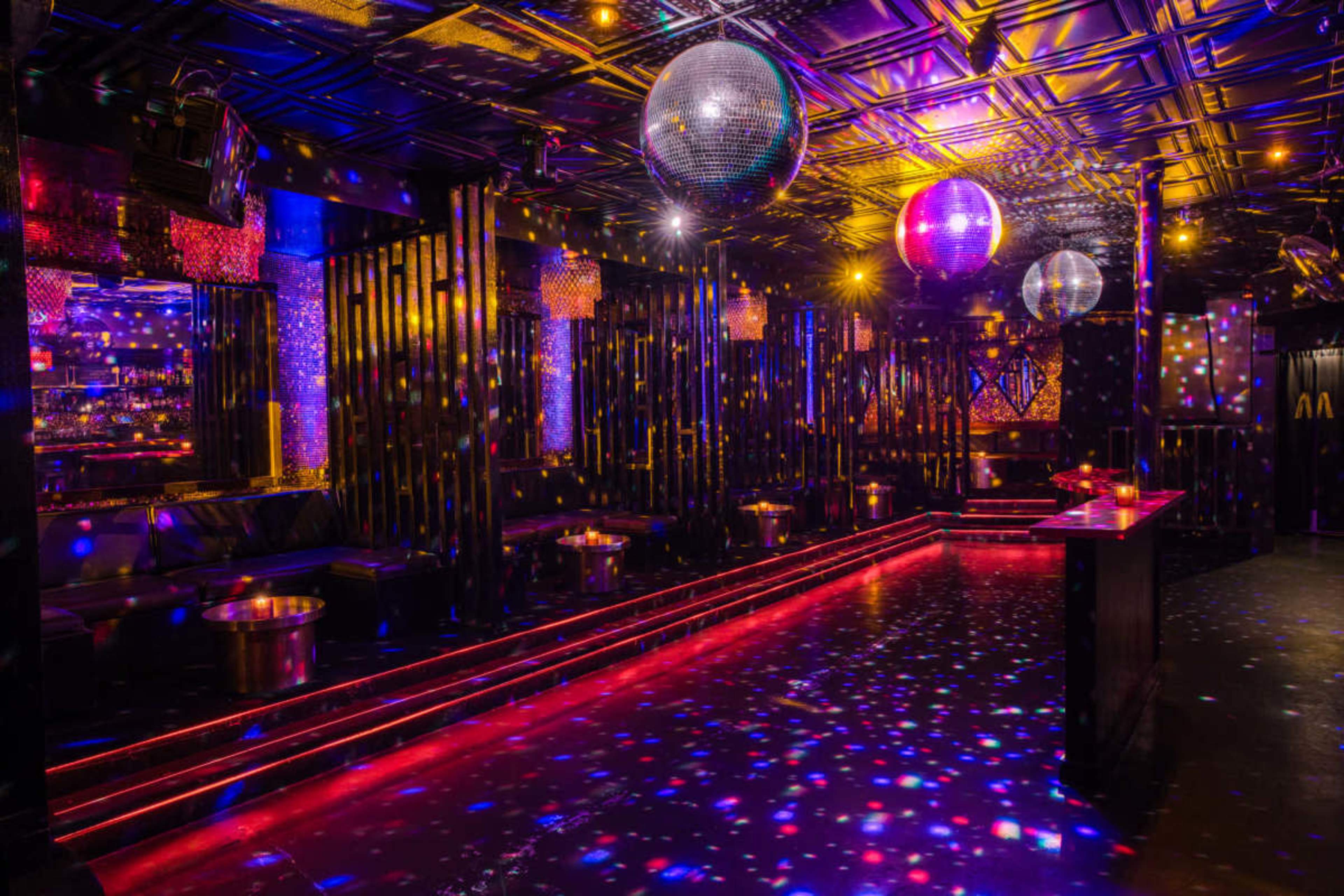 The image shows a nightclub interior with colorful lights, disco balls hanging from the ceiling, and illuminated dance floors.