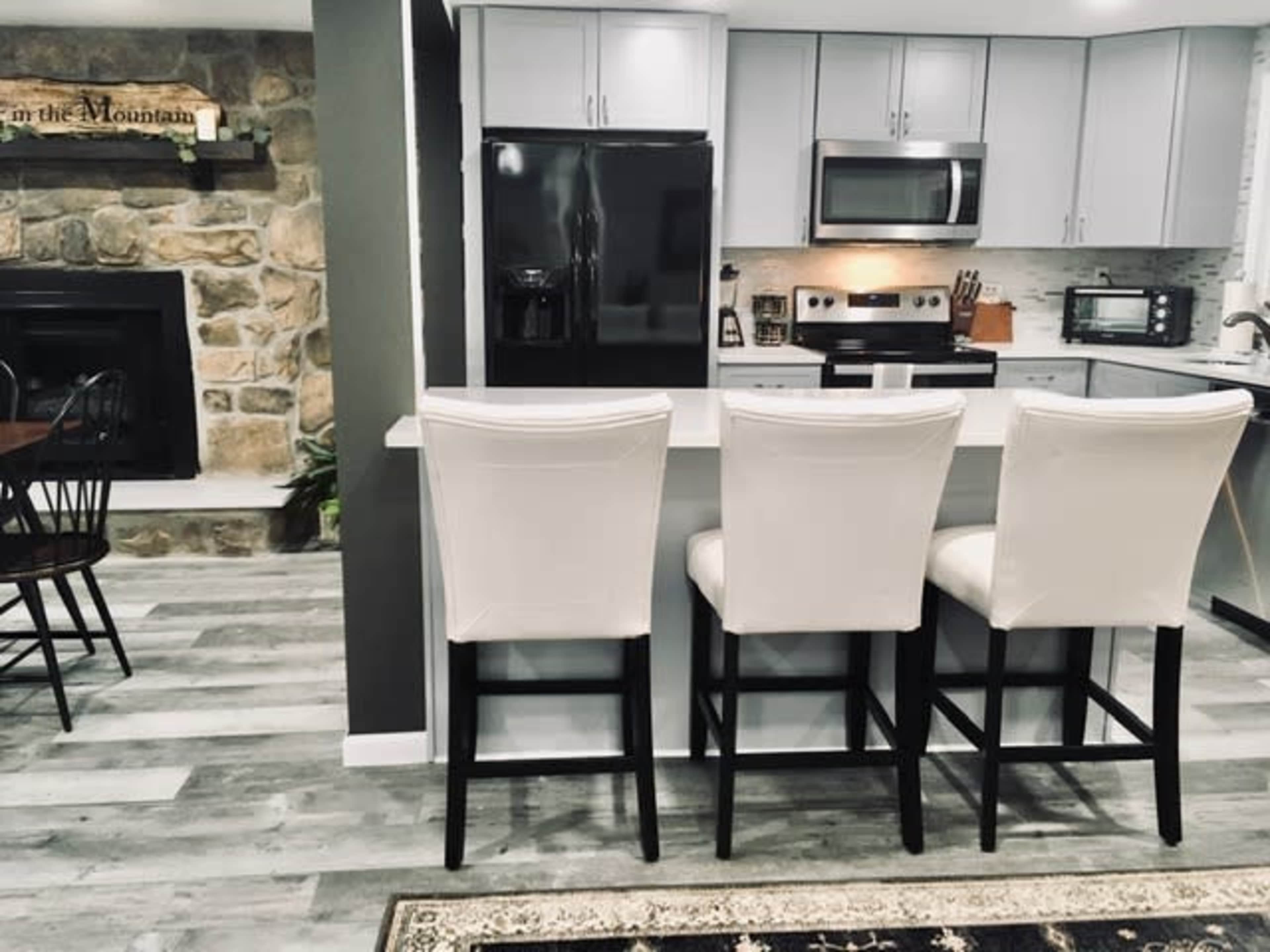 A modern kitchen with gray cabinets, a black refrigerator, and three white bar stools positioned at a countertop.