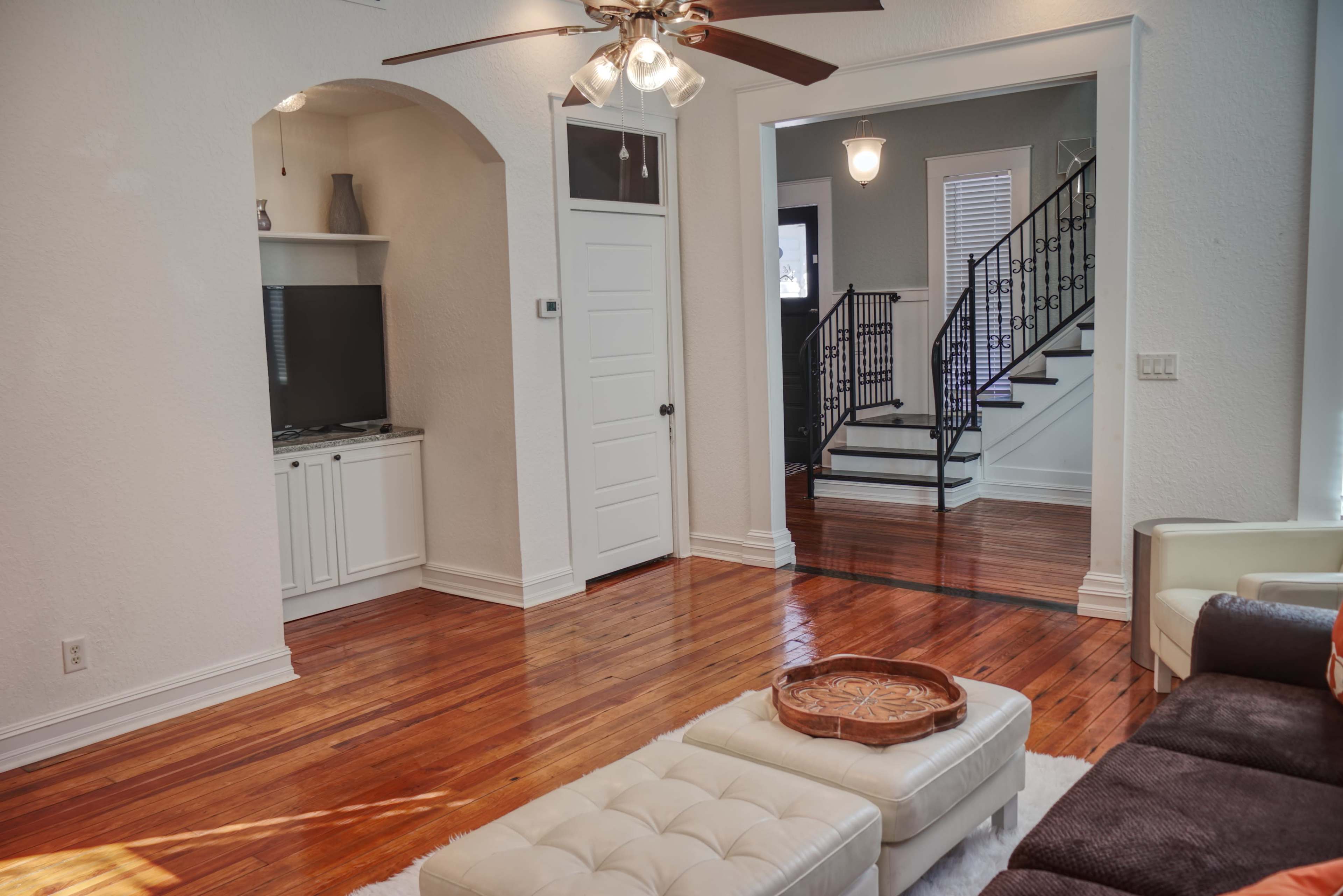 A bright living room with hardwood floors, a ceiling fan, and an open layout leading to a staircase.
