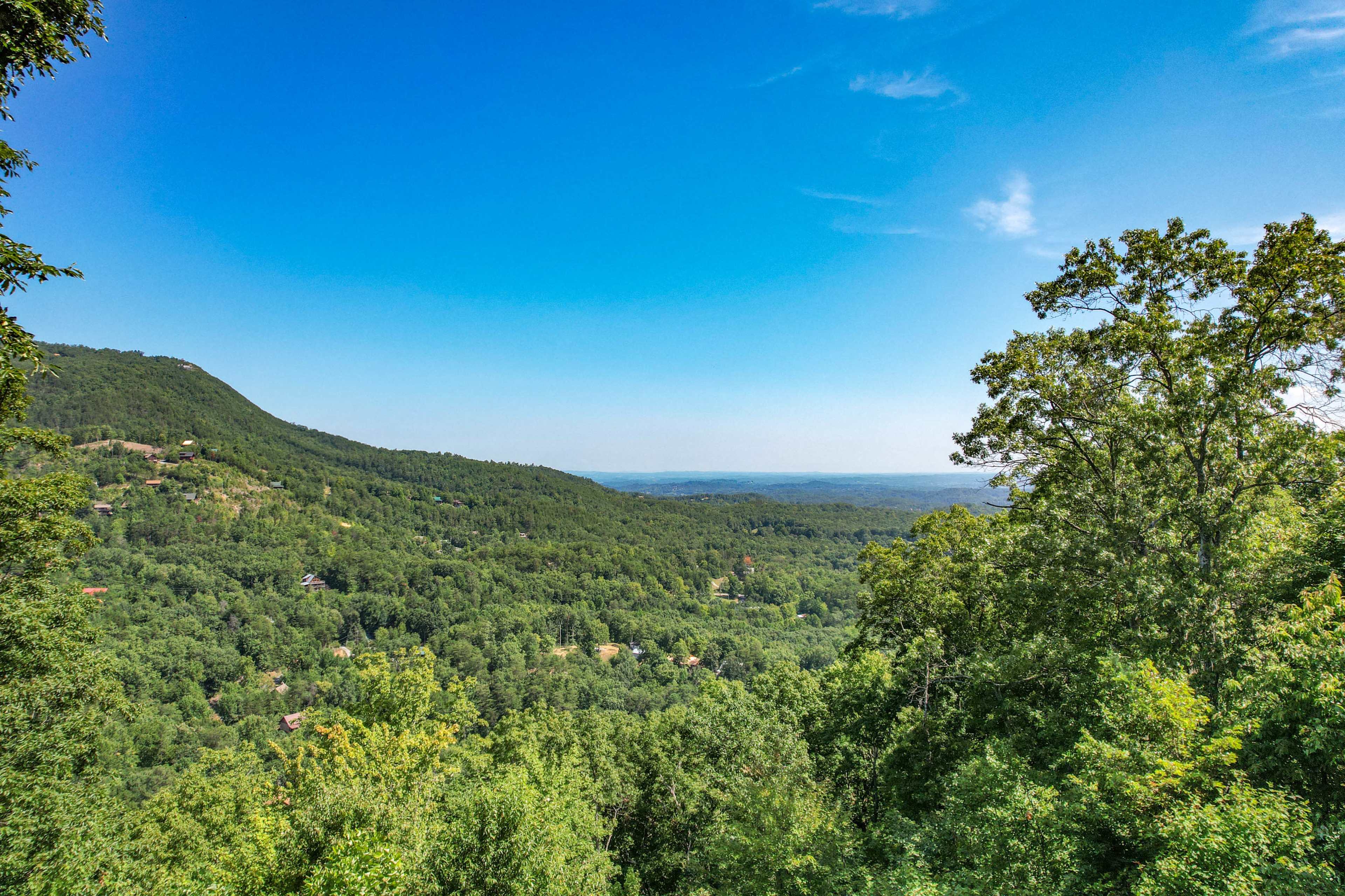 The image shows a panoramic view of a lush green mountain landscape under a clear blue sky.