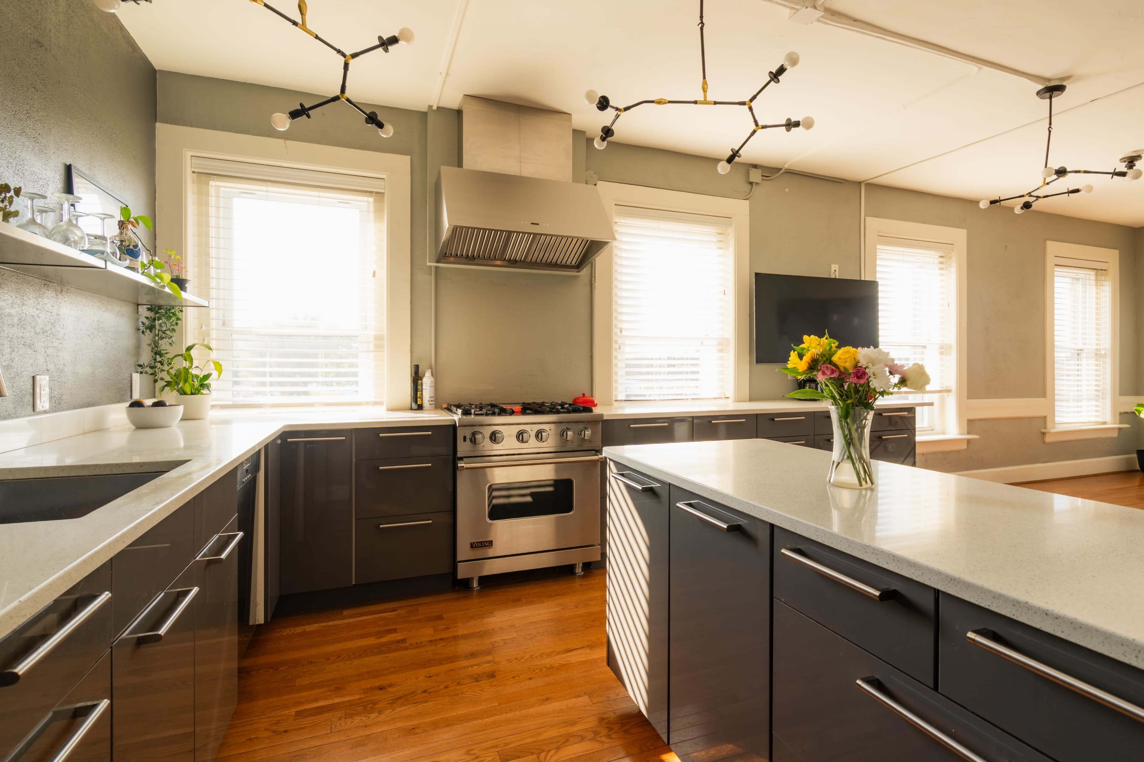 The image shows a modern kitchen featuring dark cabinetry, a stainless steel gas stove, and a large central island with a light-colored countertop.