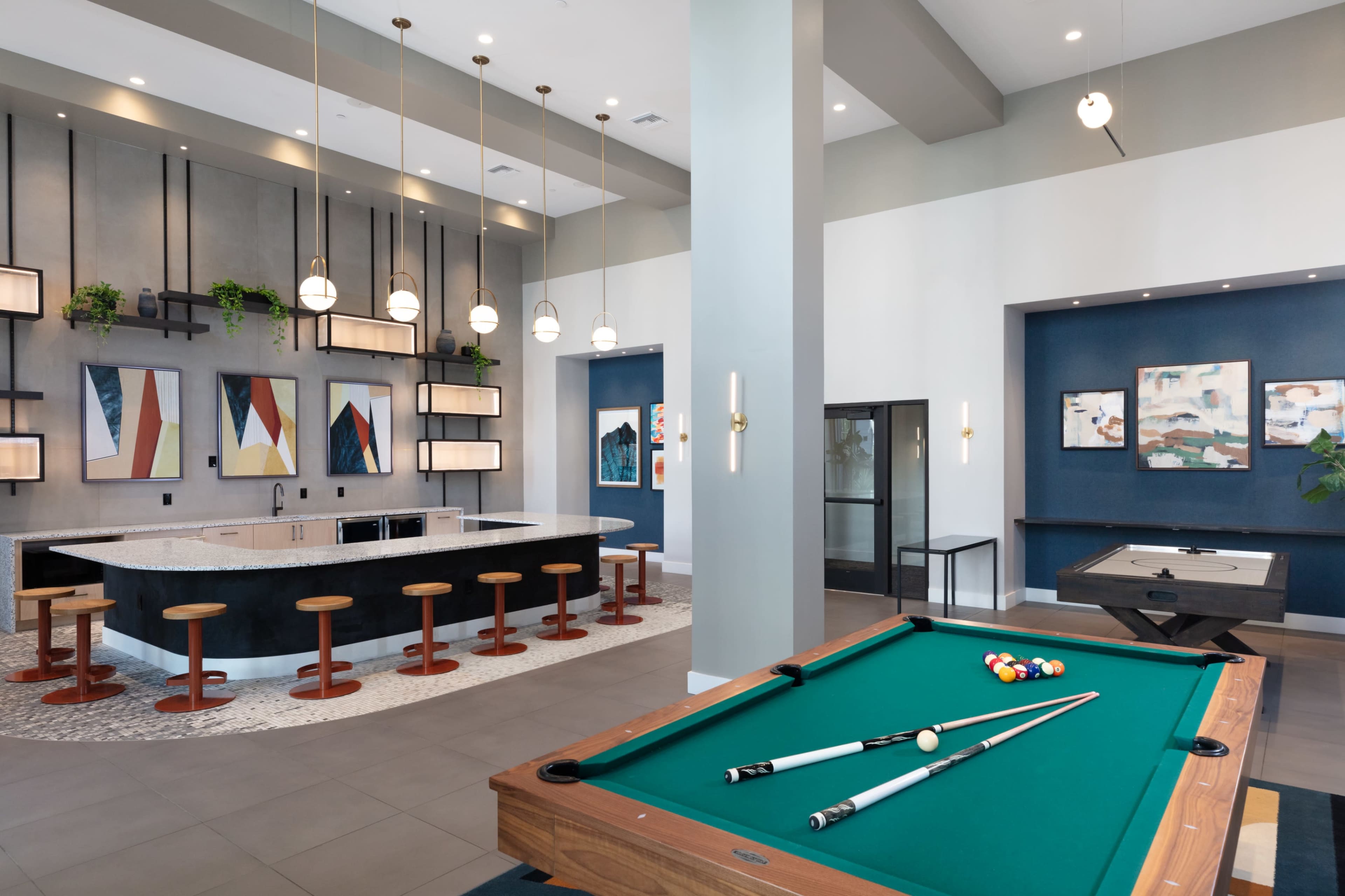 The image shows a modern game room featuring a billiard table, a wraparound bar with stools, and colorful wall art.