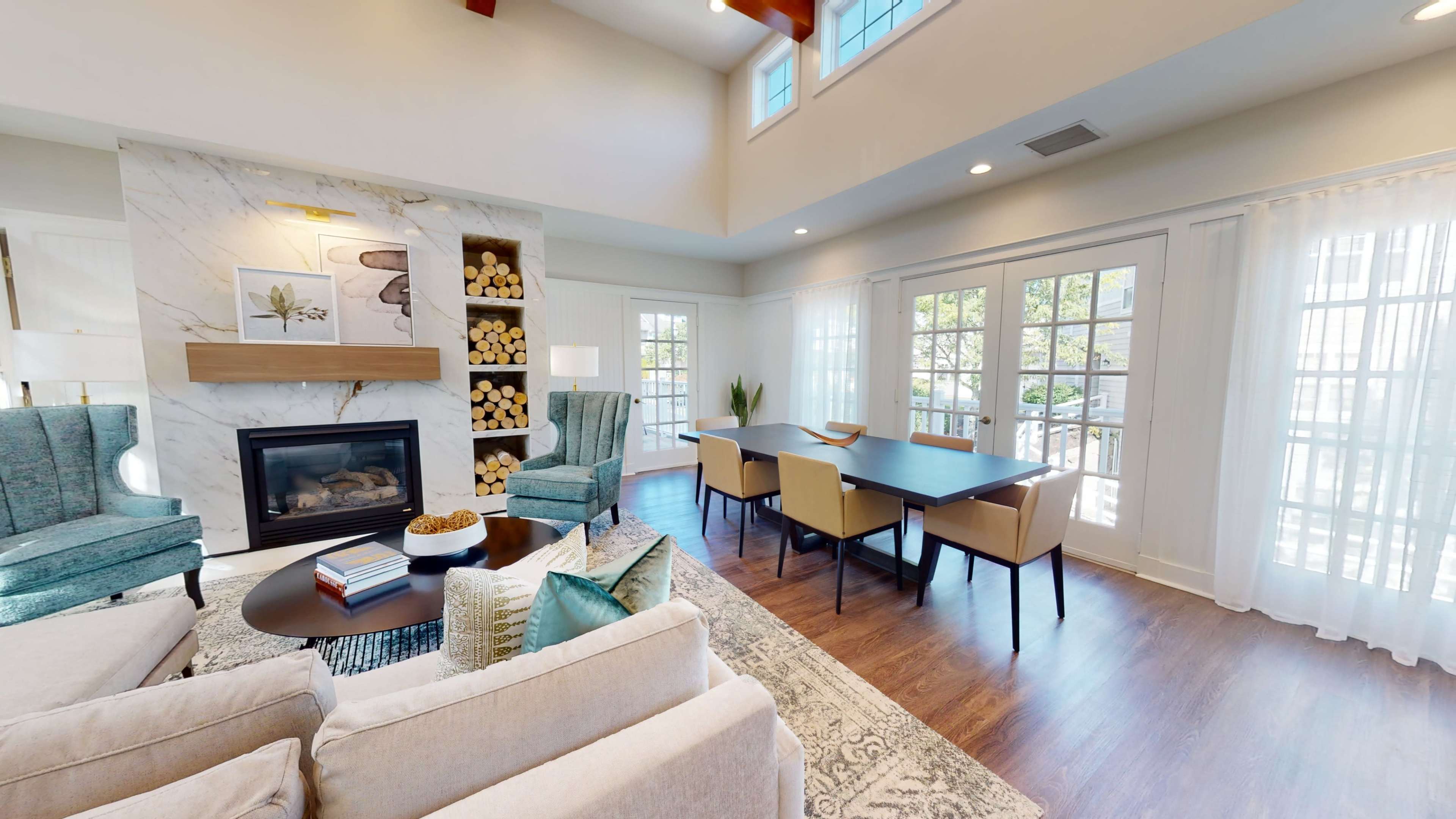 The living area features a sofa, two armchairs, a coffee table, and a dining table, with a fireplace and stacked wood display in the background.