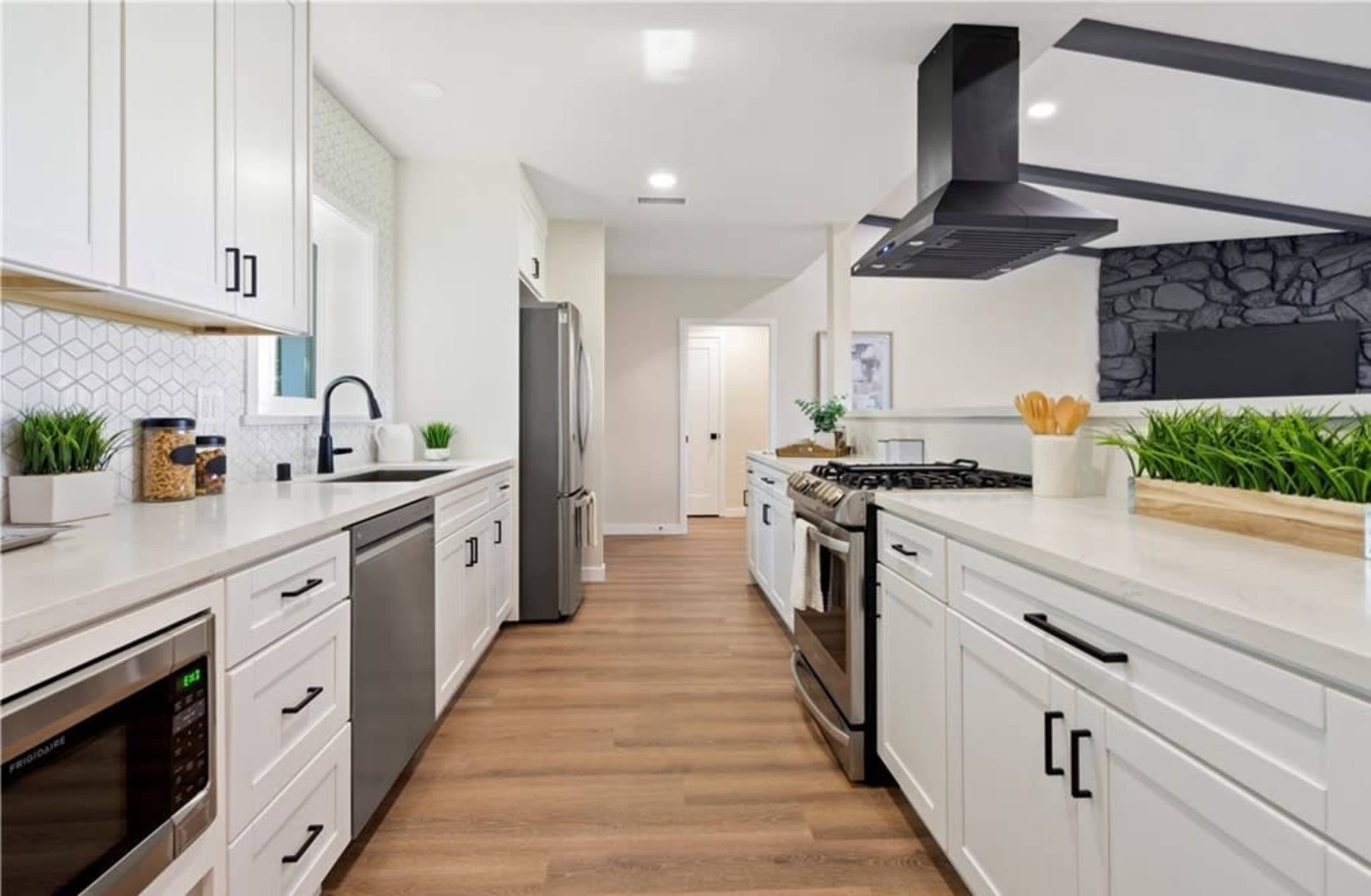 A modern kitchen features white cabinetry, stainless steel appliances, and a large island with a stone accent wall.