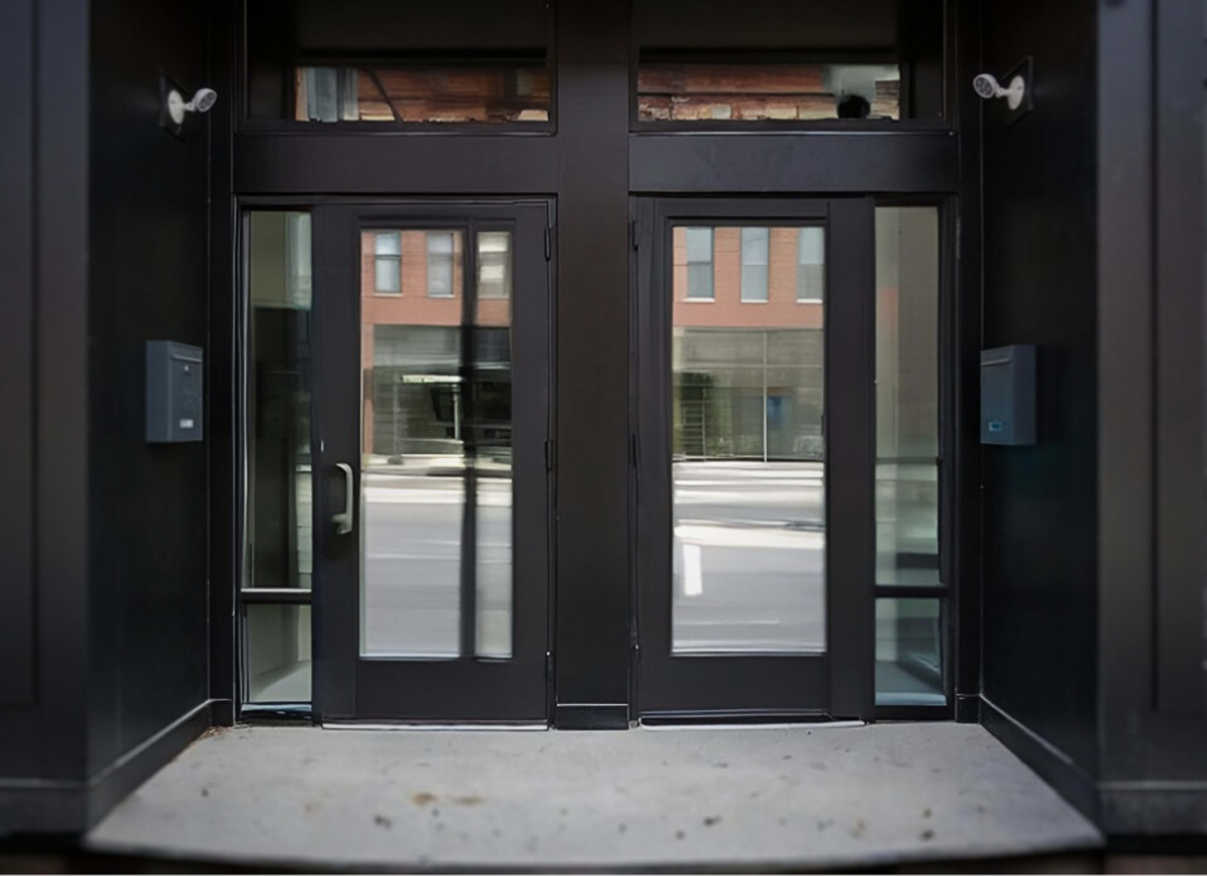 The image shows a pair of glass double doors at a modern building entrance, with mailboxes mounted on the wall beside them.