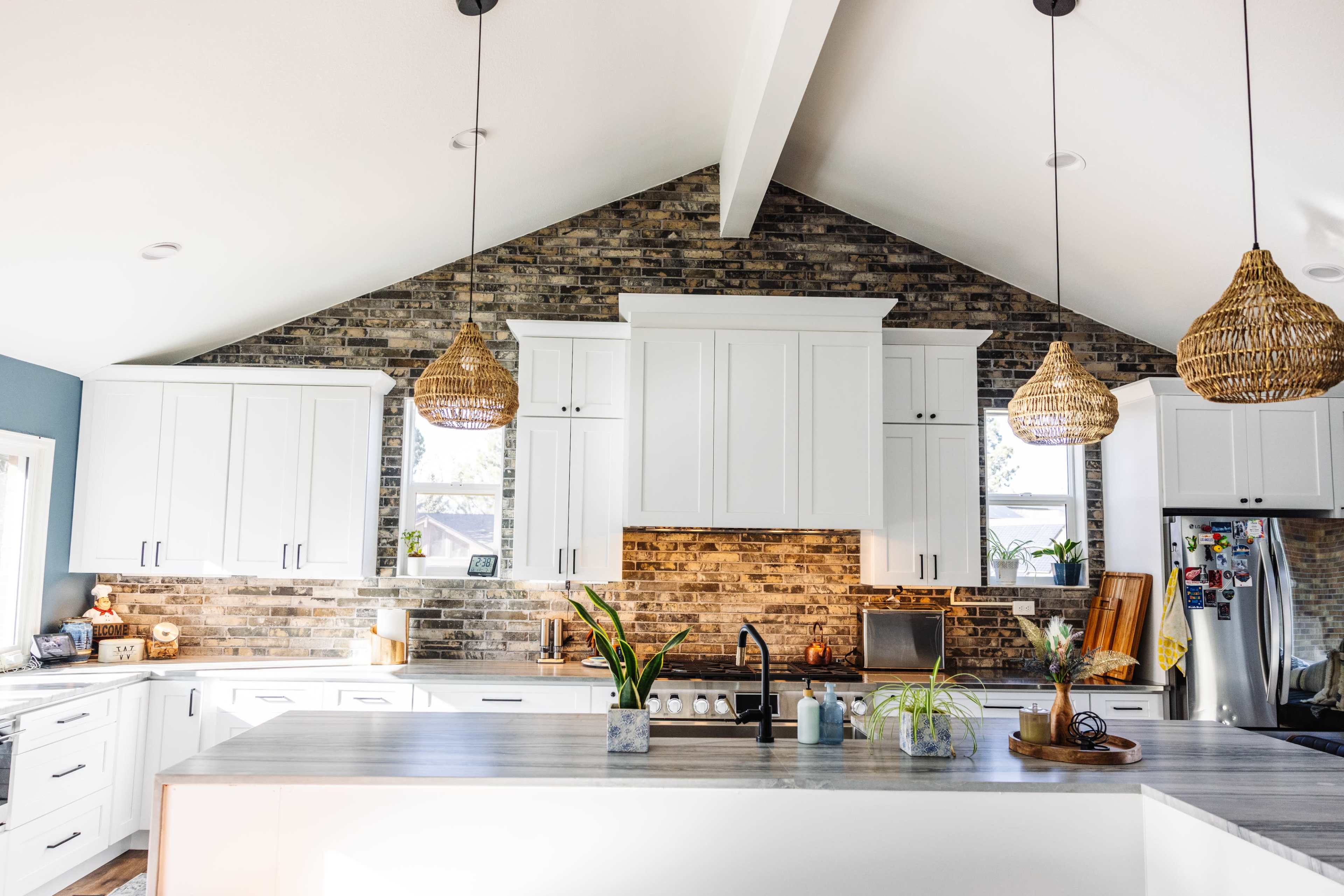 The image shows a modern kitchen with white cabinetry, a stone backsplash, and a large island featuring pendant lighting.