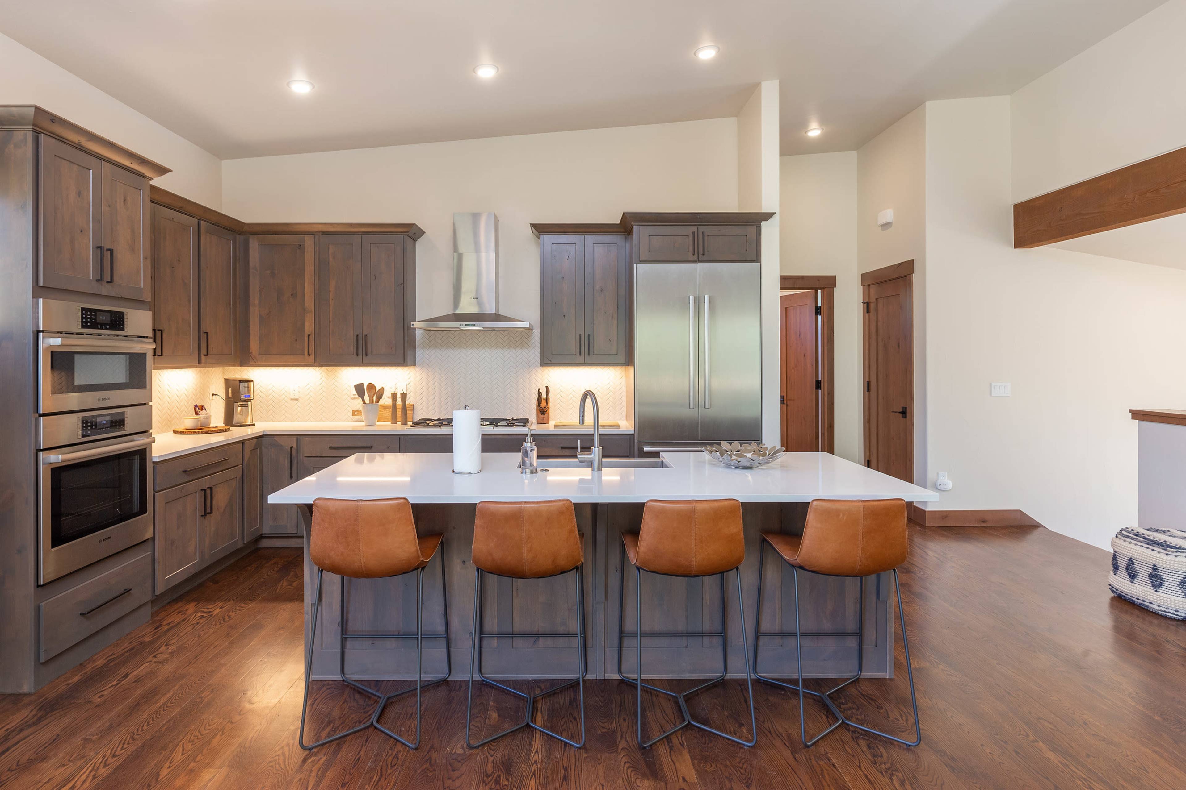 A modern kitchen features wooden cabinets, stainless steel appliances, a central island with seating, and warm lighting.