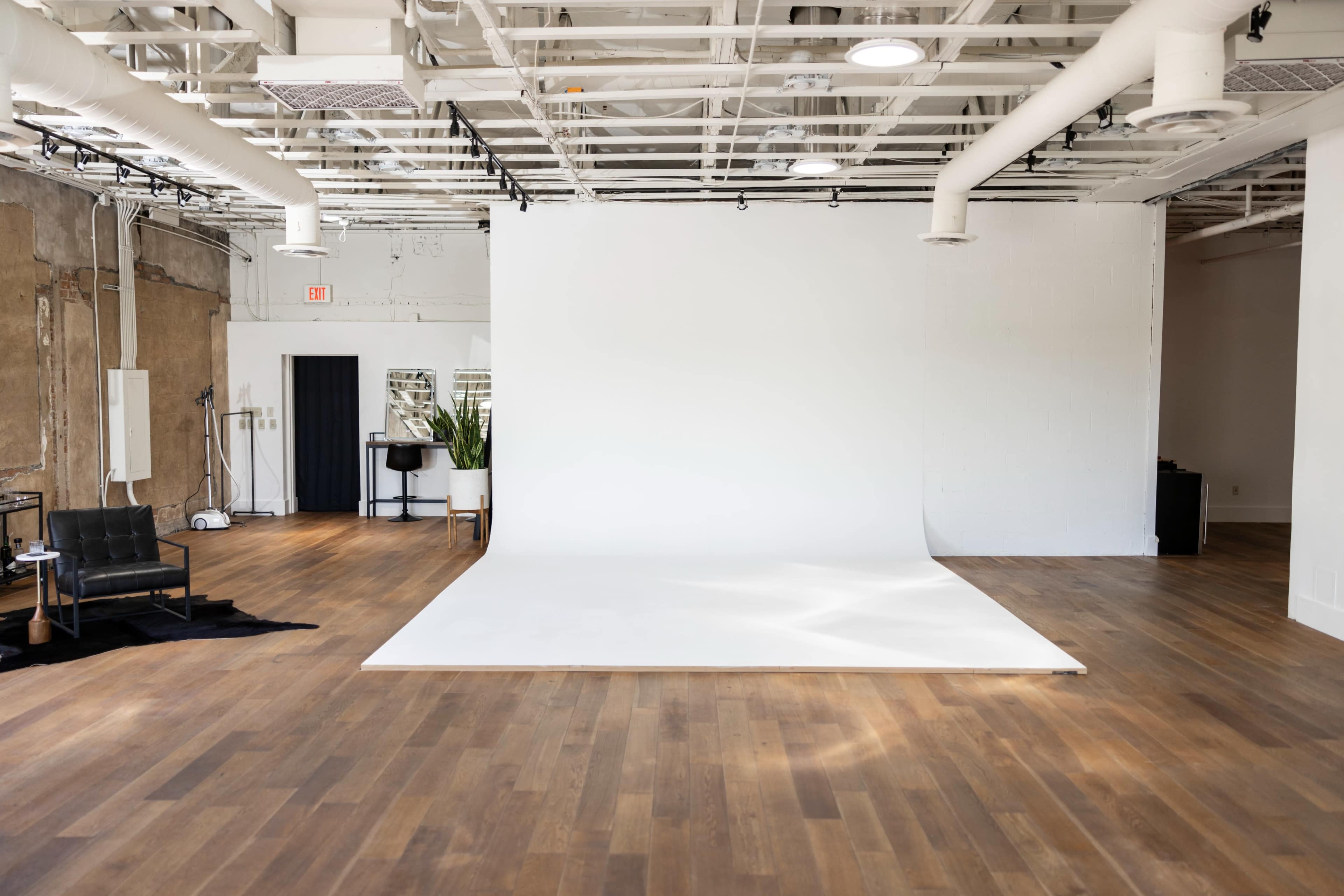 A spacious photography studio with a large white backdrop, wooden flooring, and minimal furniture.