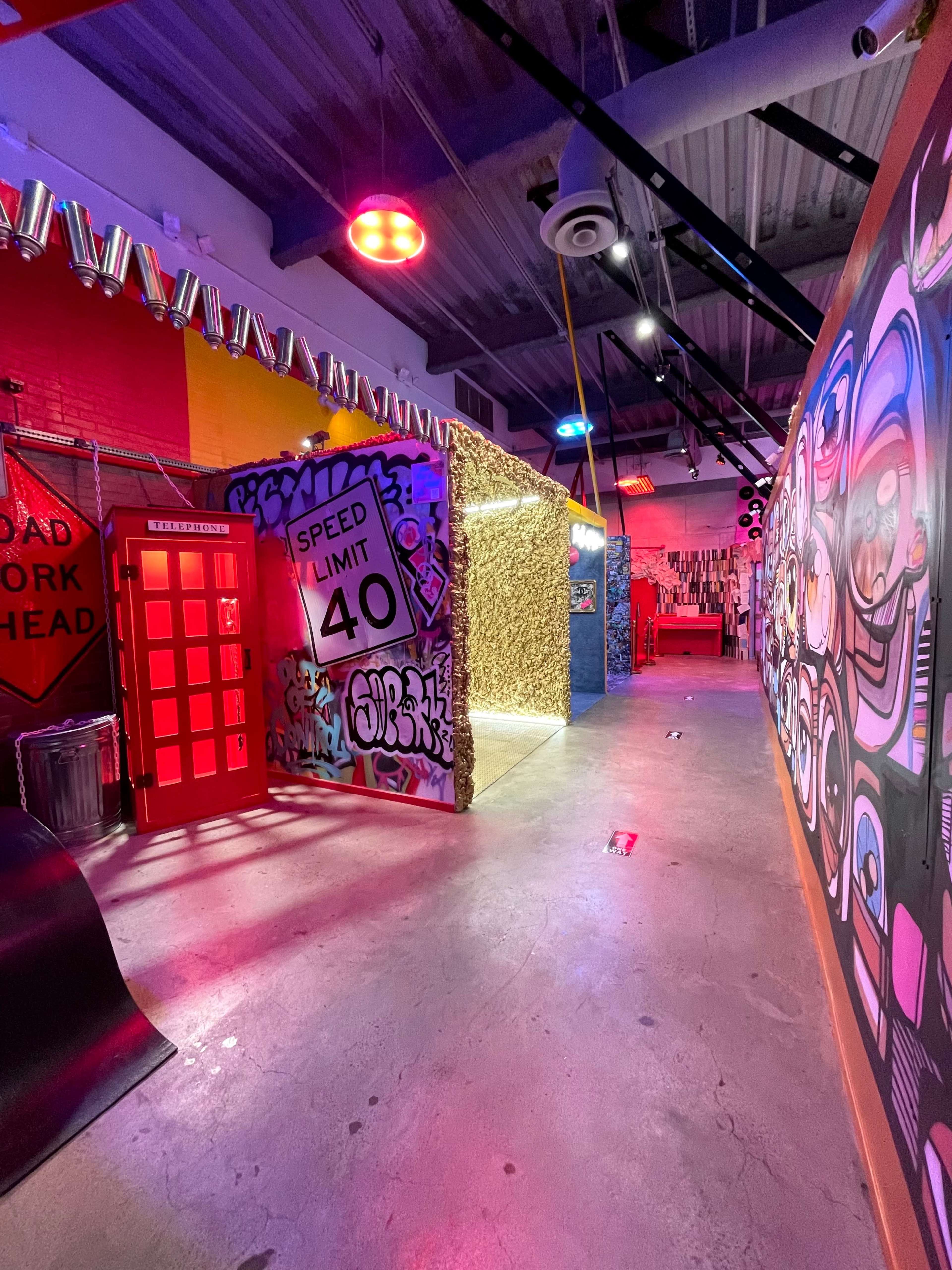 A vibrant corridor featuring colorful graffiti walls, a red telephone booth, and illuminated overhead lights.