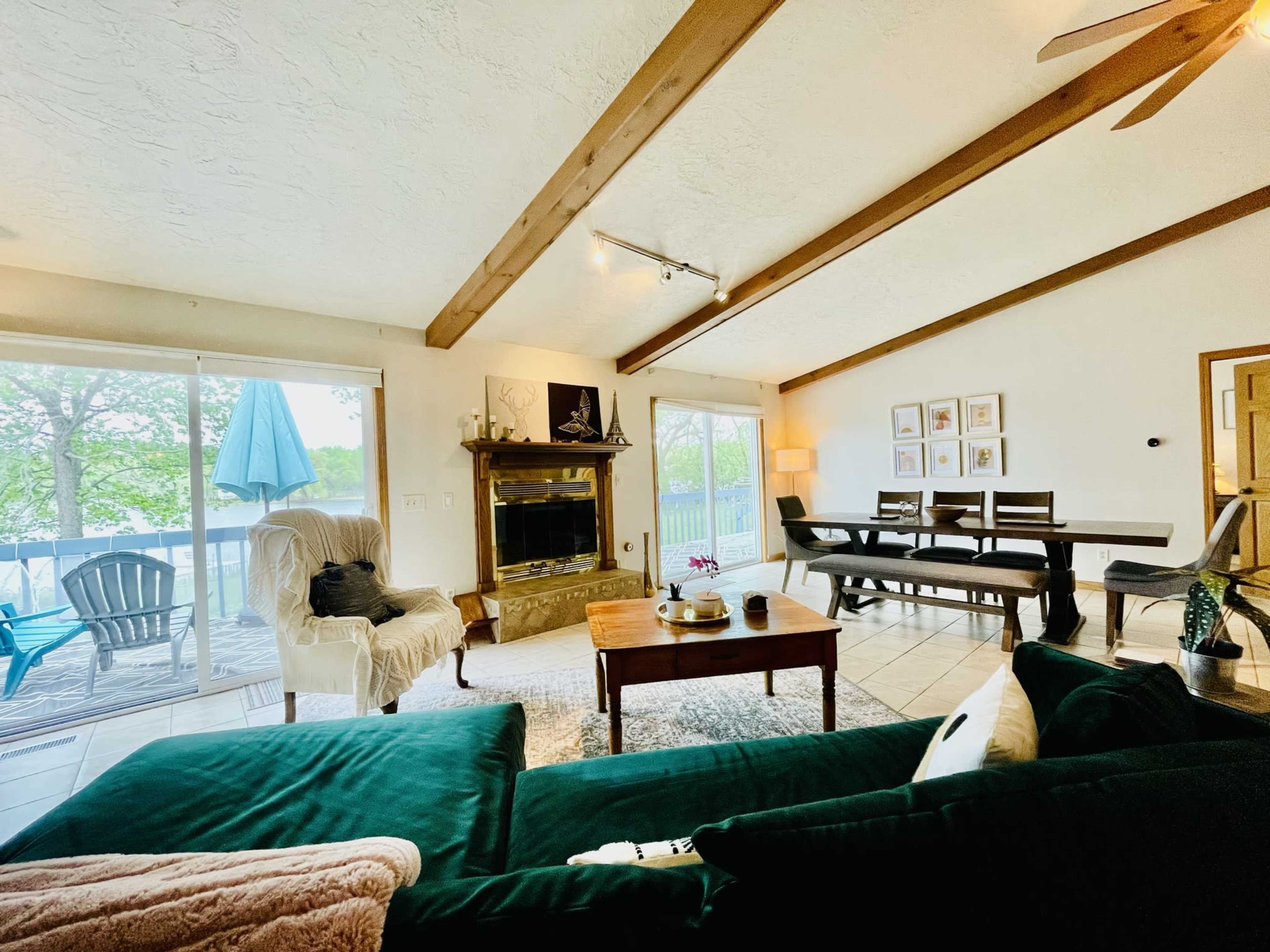 The living room features a sofa, a coffee table, a fireplace with a mantel, and dining space with sliding glass doors opening to a deck.