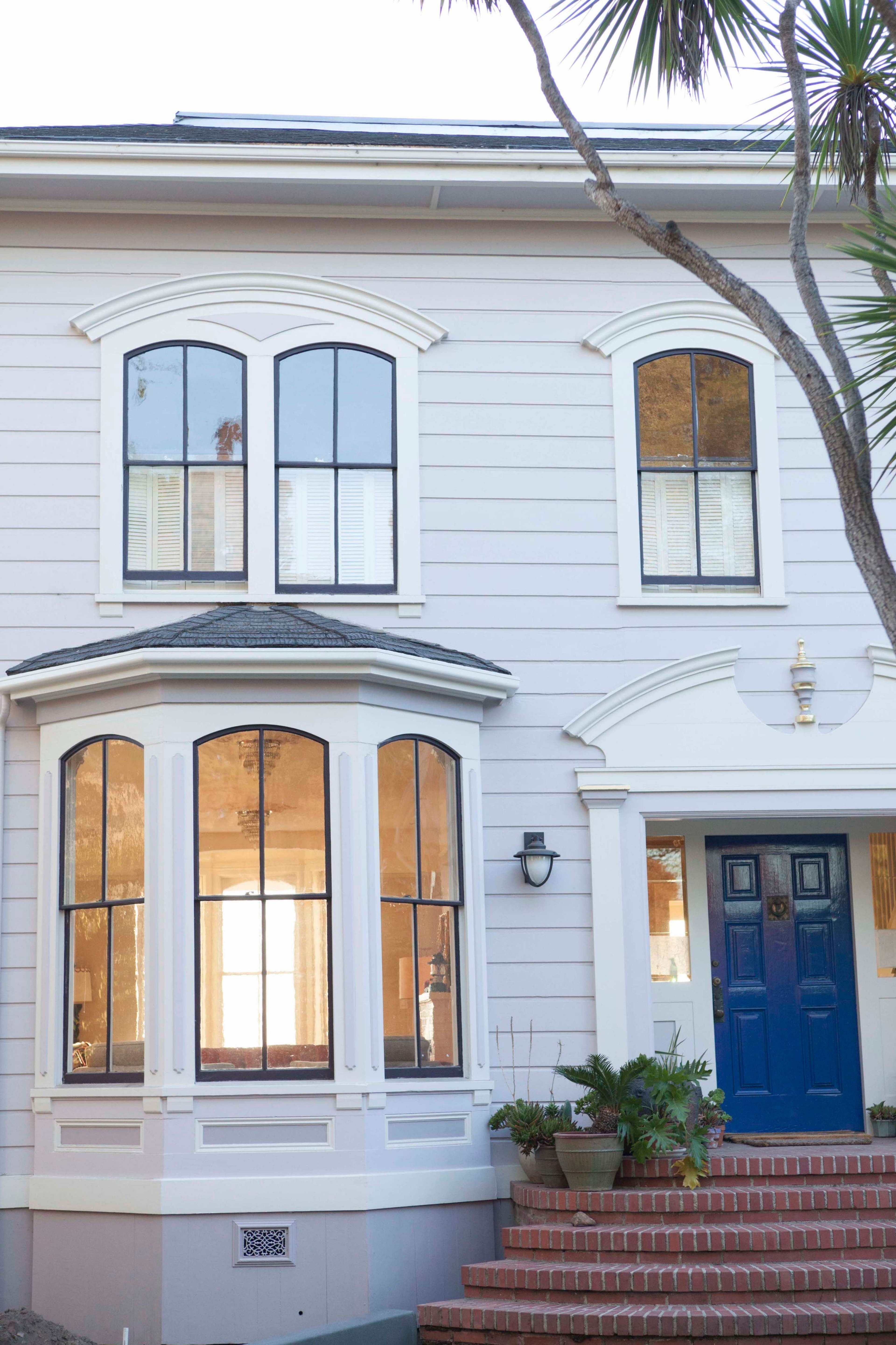 A two-story house with large, arched windows, a blue front door, and a set of brick stairs leading to the entrance.