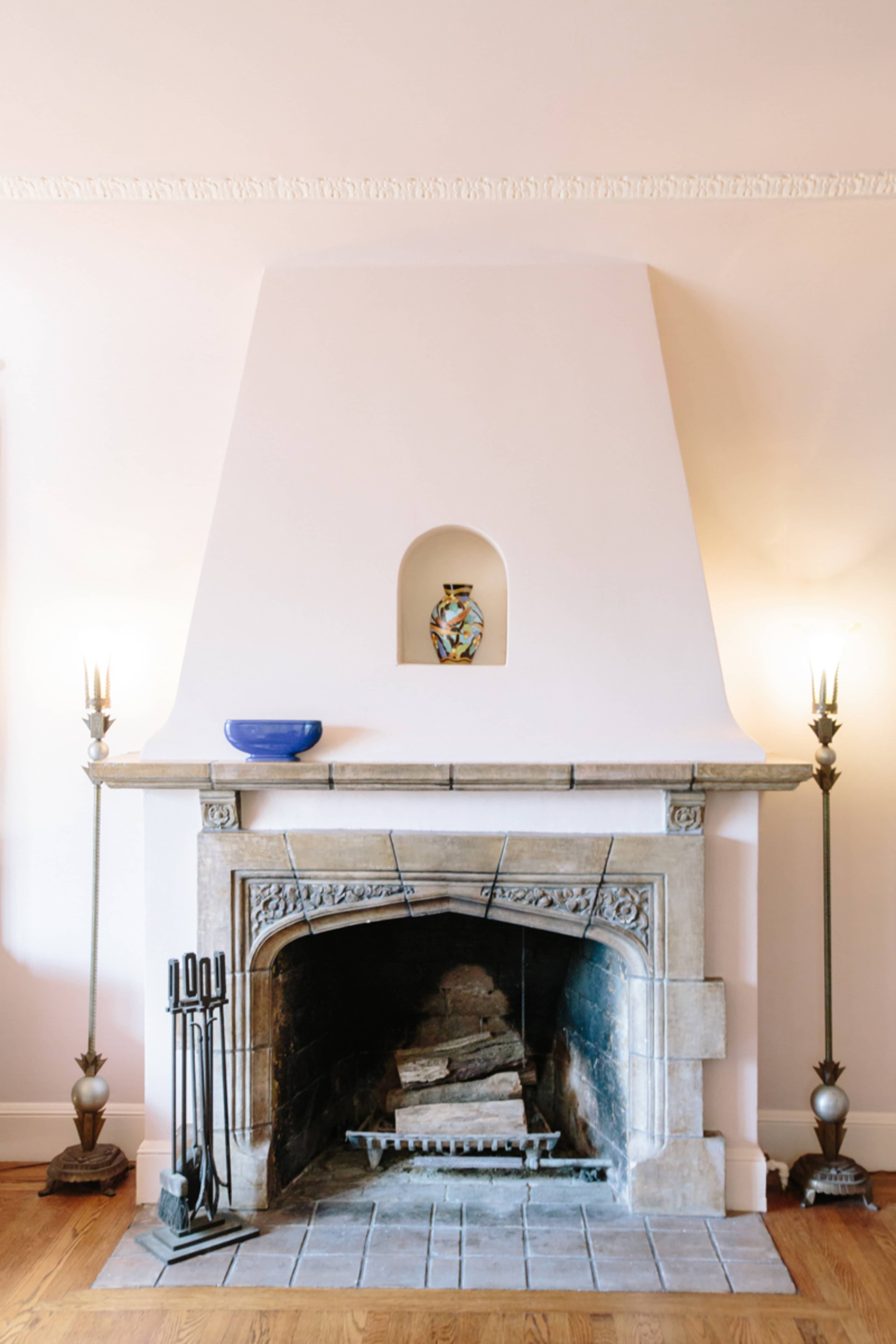 A white fireplace with a decorative niche holds a small vase, flanked by two tall candleholders on either side.