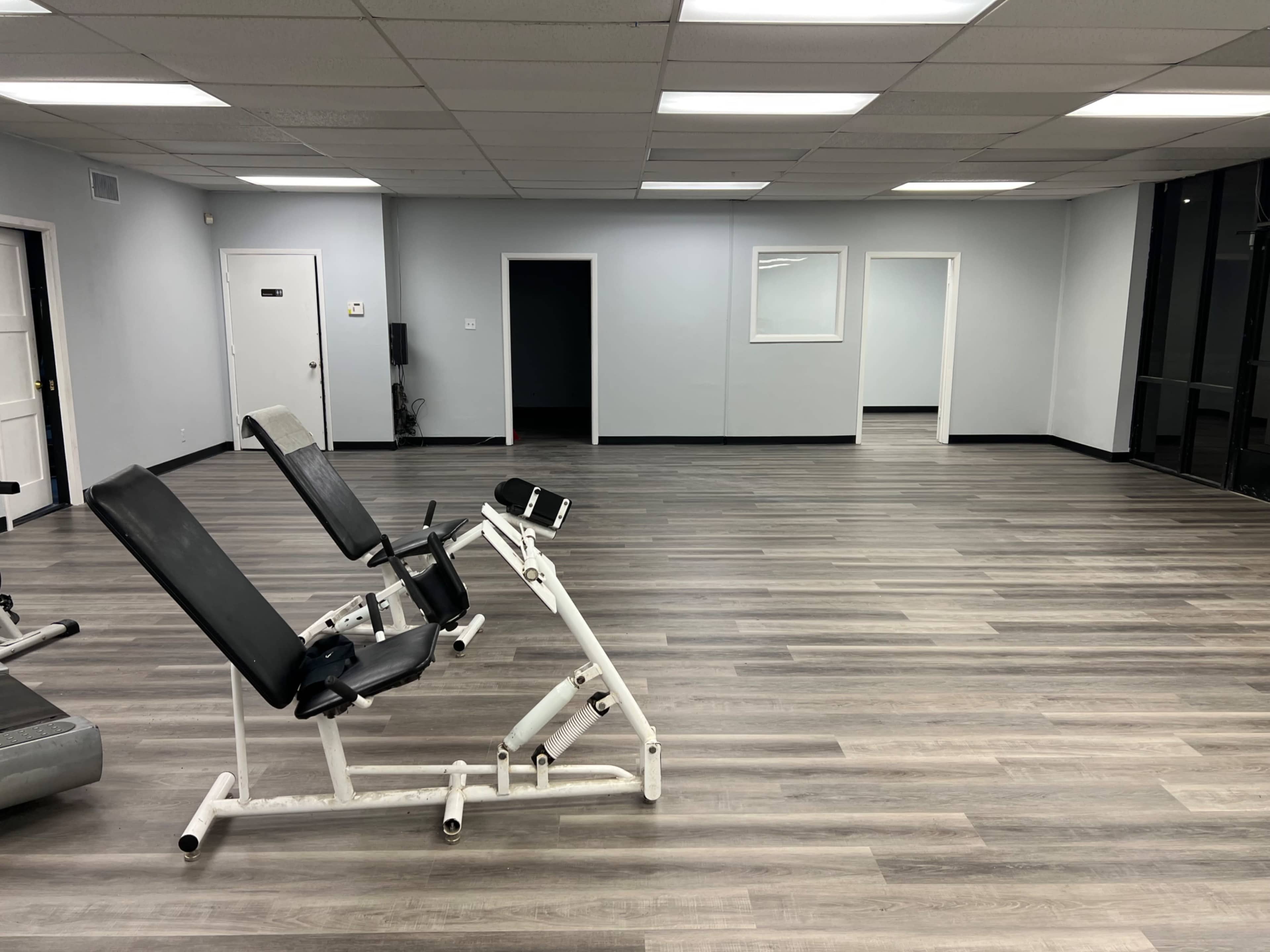 The image shows an empty gym interior with exercise equipment and wooden flooring.