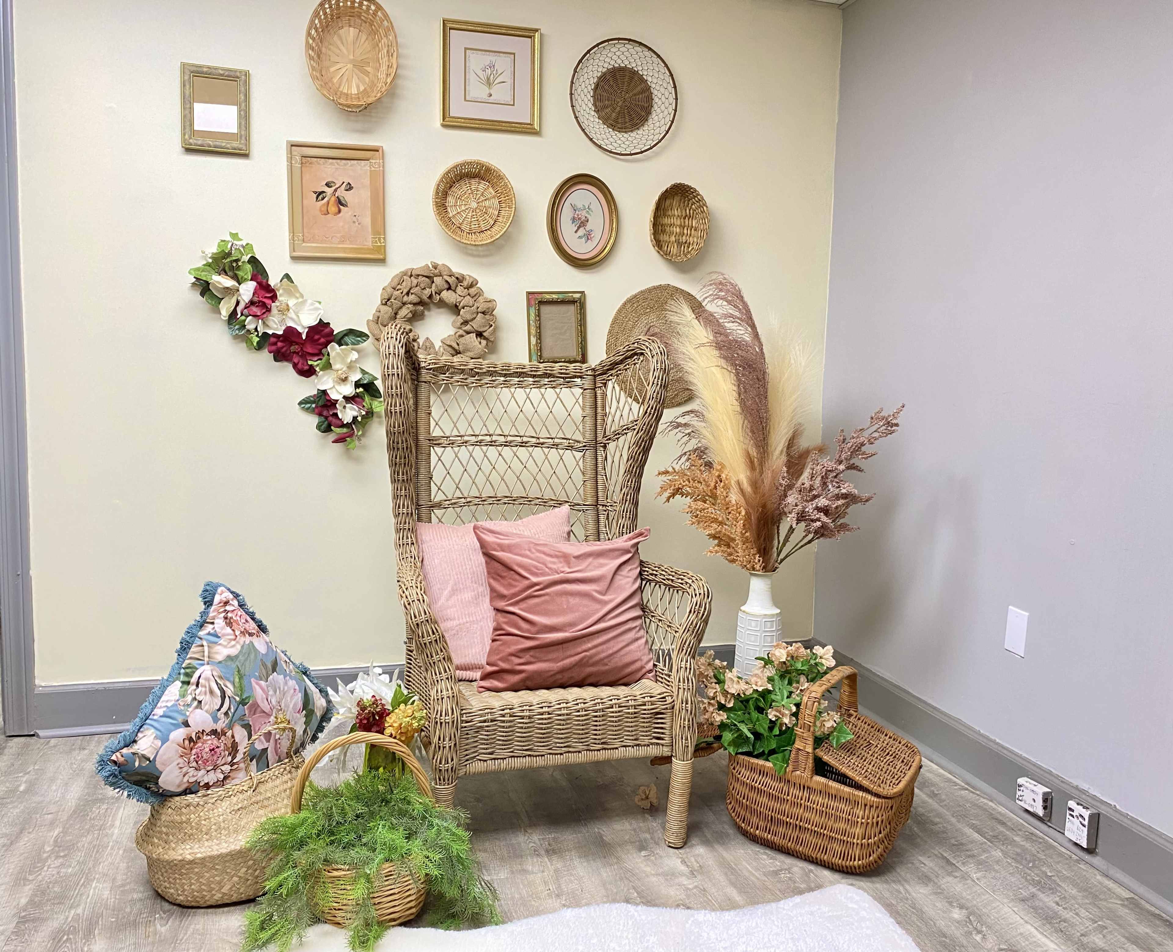 A decorative corner featuring a wicker chair surrounded by various wall art, floral arrangements, and woven baskets.