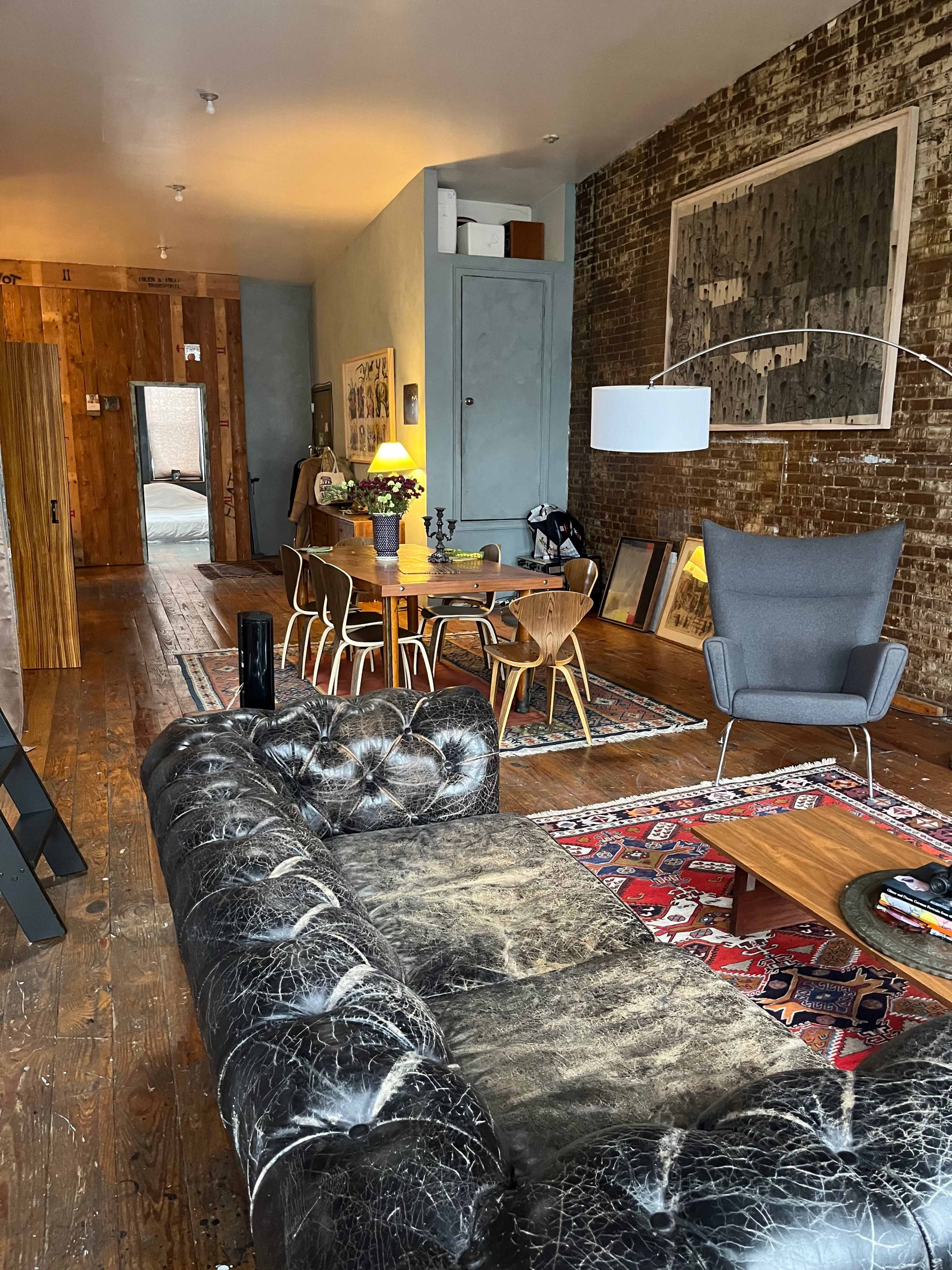 A stylish living space featuring a leather sofa, a wooden dining table with chairs, and exposed brick walls.