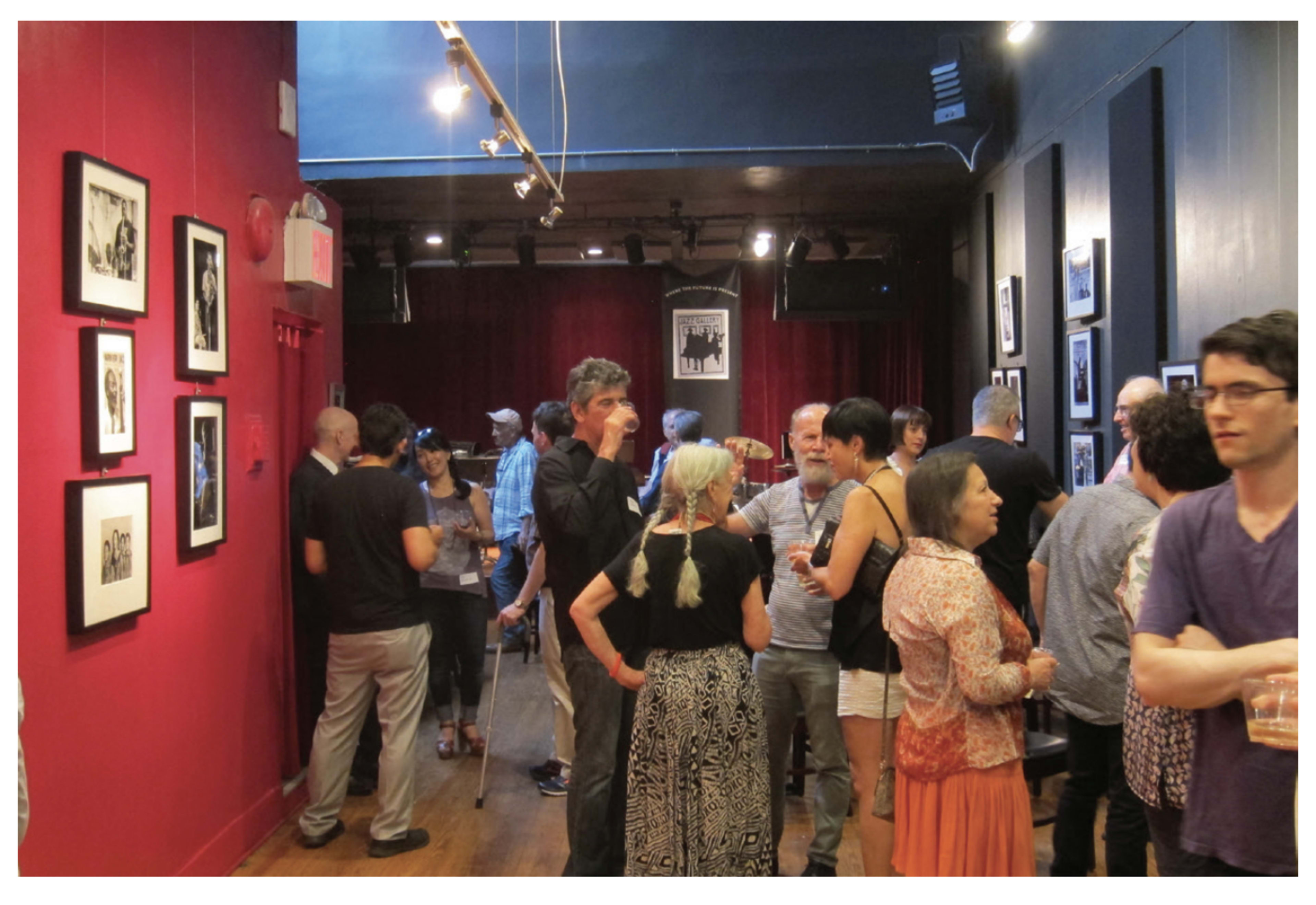 A group of people socialize in a dimly lit room adorned with framed photographs on the walls.