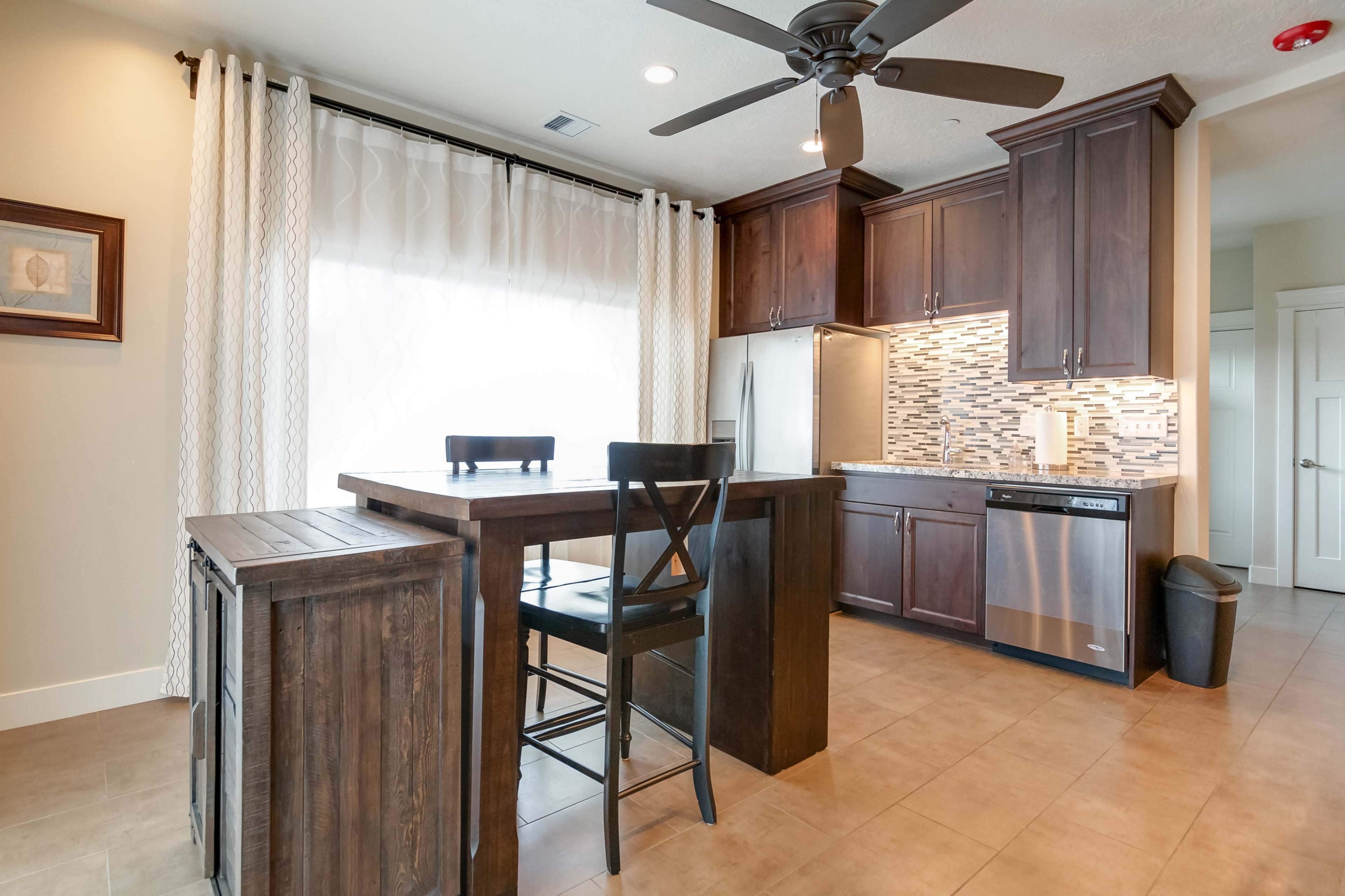 A modern kitchen features dark wooden cabinets, a tiled backsplash, and a small dining table with two black chairs.