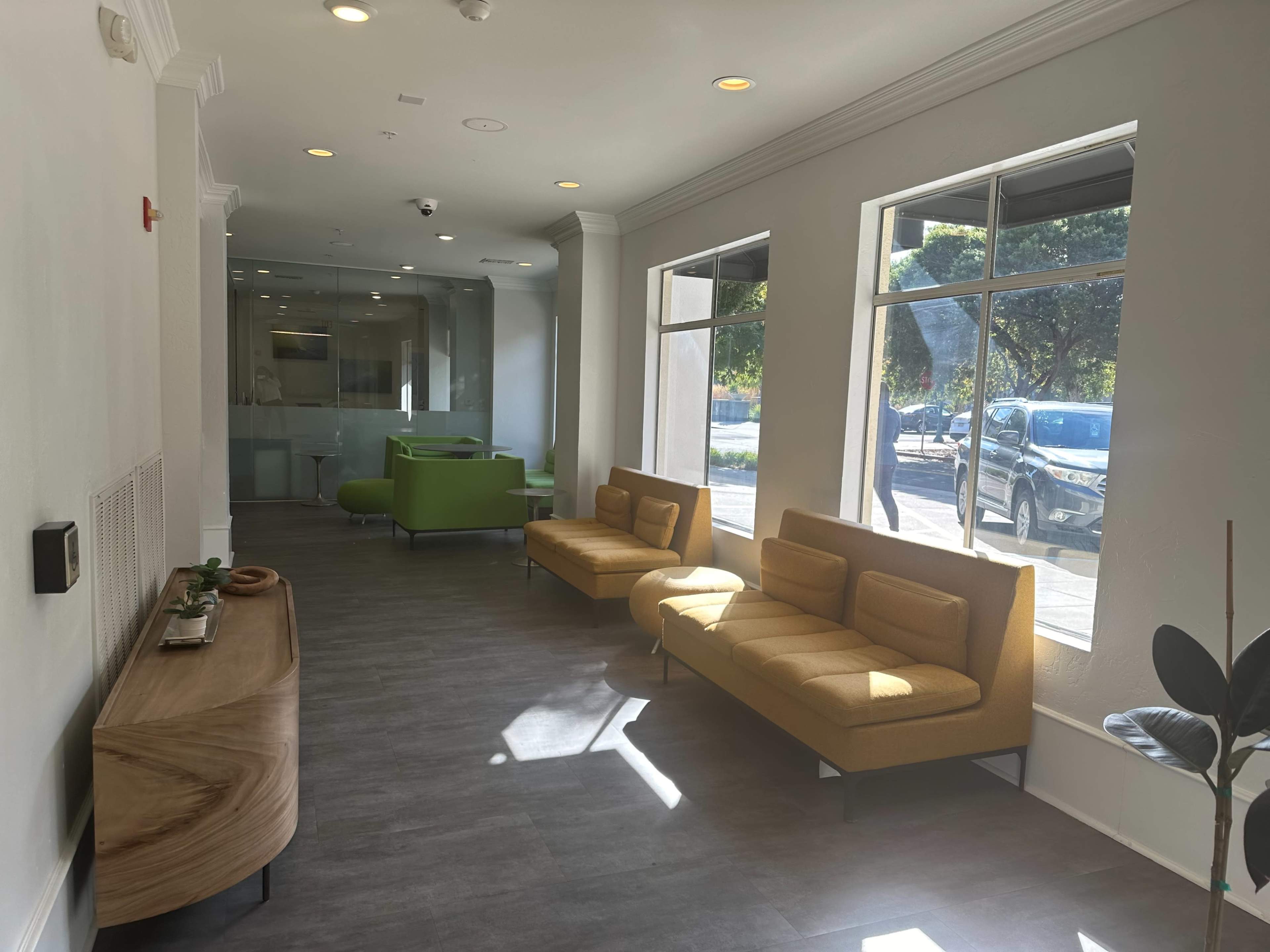 A modern waiting area with two sofas, a wooden side table, and large windows allowing natural light to enter.
