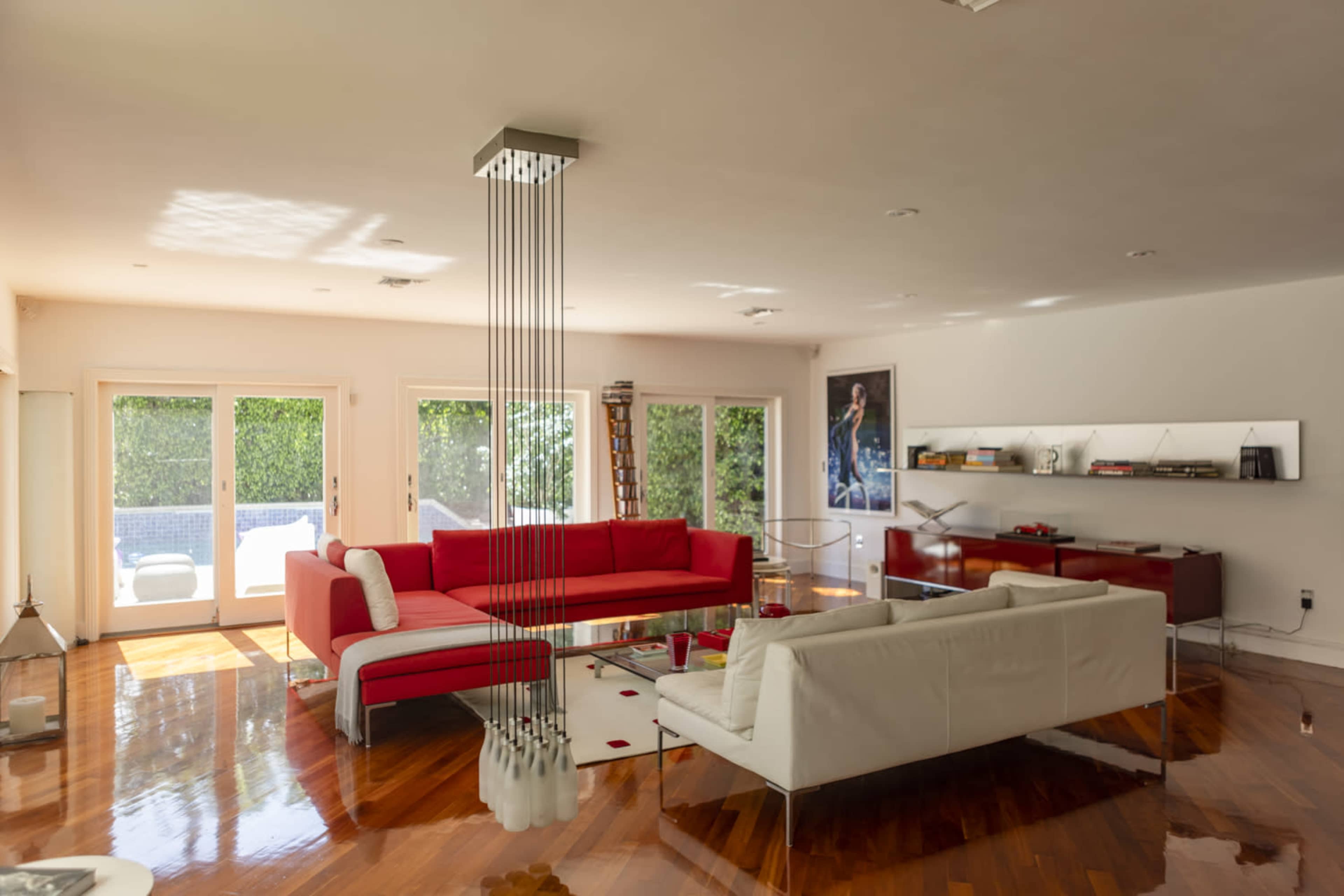 The image shows a modern living room with red and white sofas, large windows, and polished wooden floors.