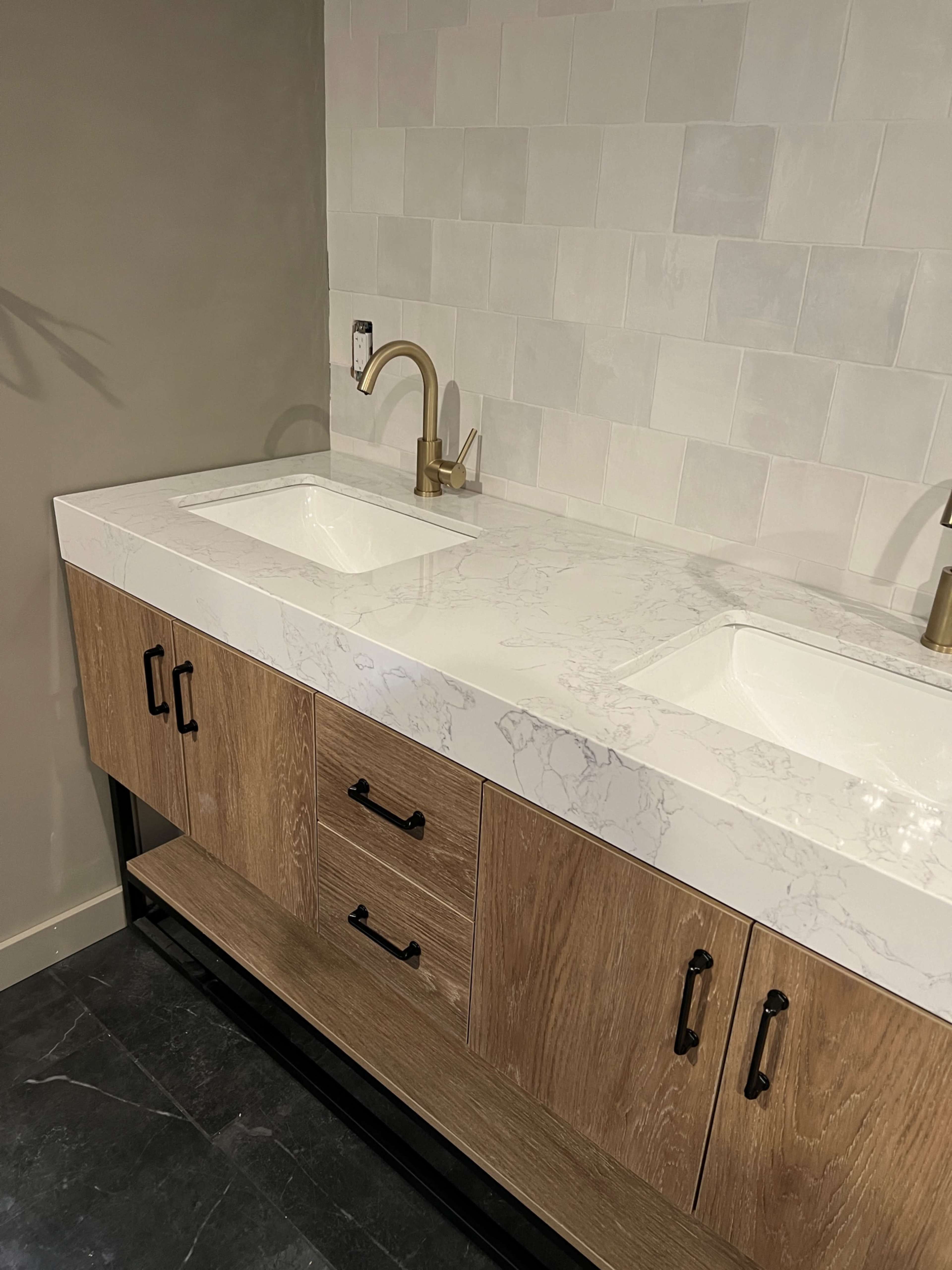 The image shows a modern bathroom vanity with a marble countertop, two sinks, and wooden cabinetry below.