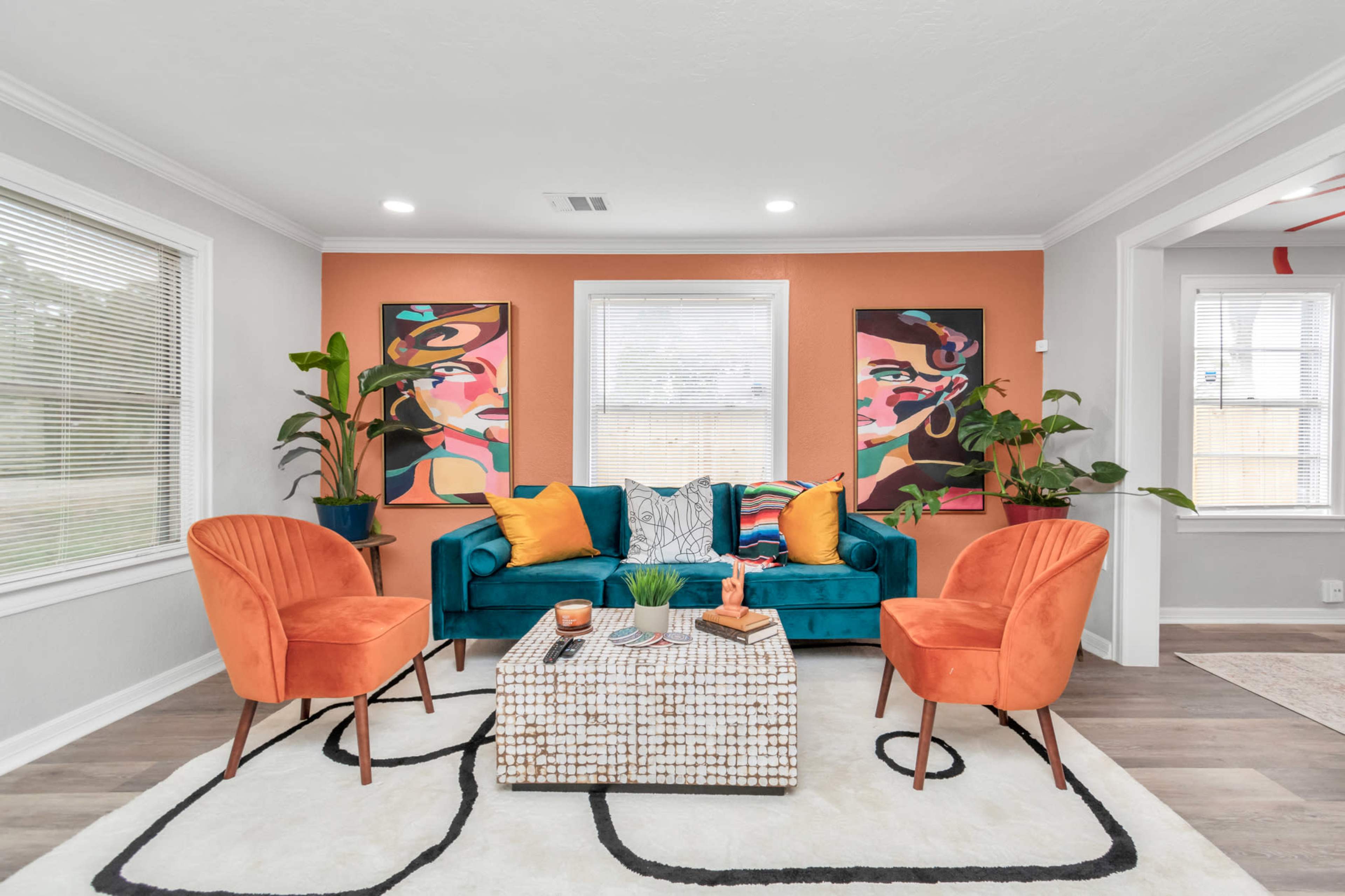The living room features a teal sofa, two orange chairs, a patterned rug, and vibrant artwork on the walls.